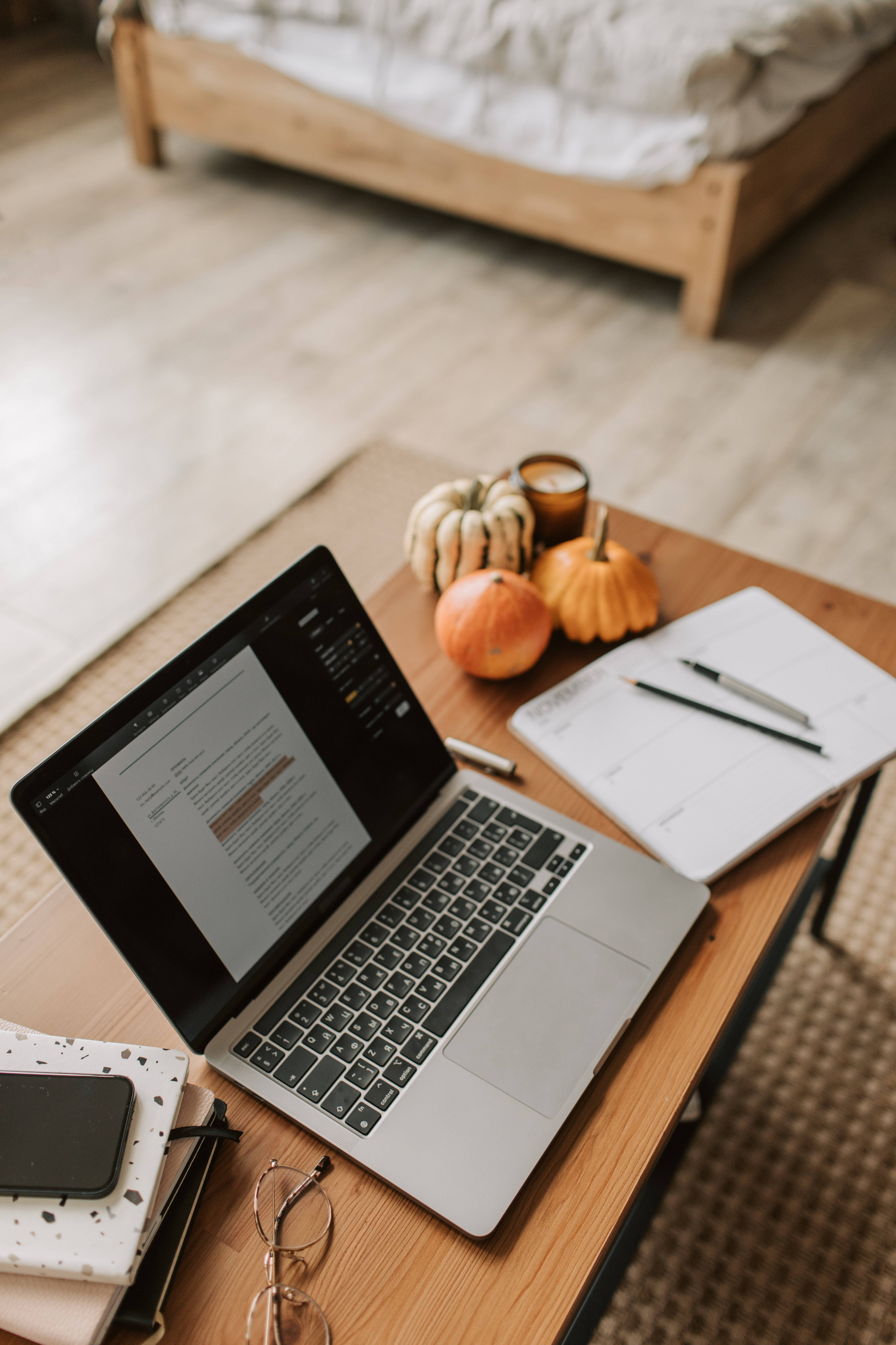 aesthetic tumblr laptop 桌布 壁紙 — 舒適的臥室書桌設置，配有筆記型電腦、筆記本、南瓜和眼鏡，沐浴在溫暖的自然光中。