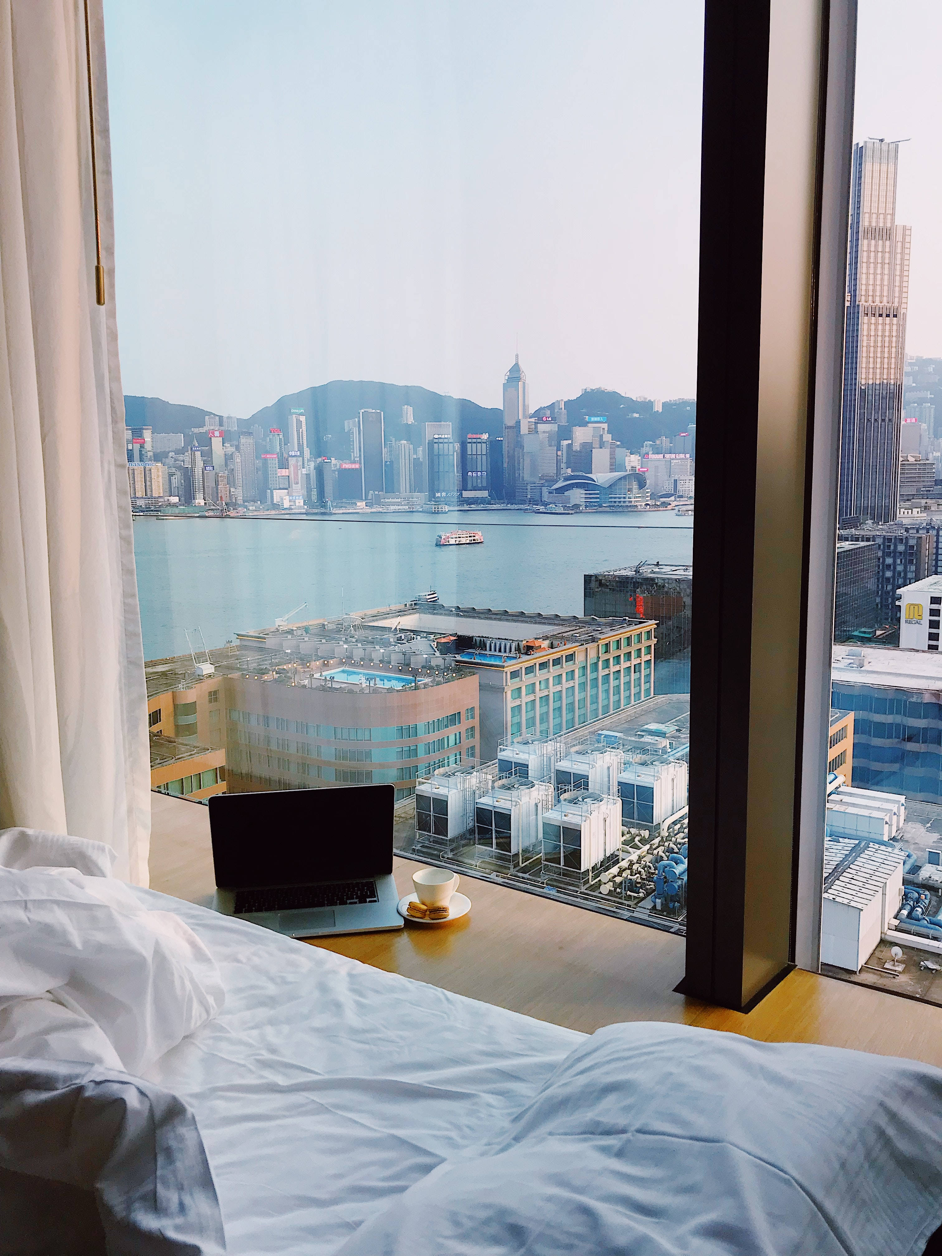 Hotel 桌布 壁紙 — 舒適的飯店房間，窗台上放著筆記型電腦和咖啡，俯瞰香港的天際線和港口。