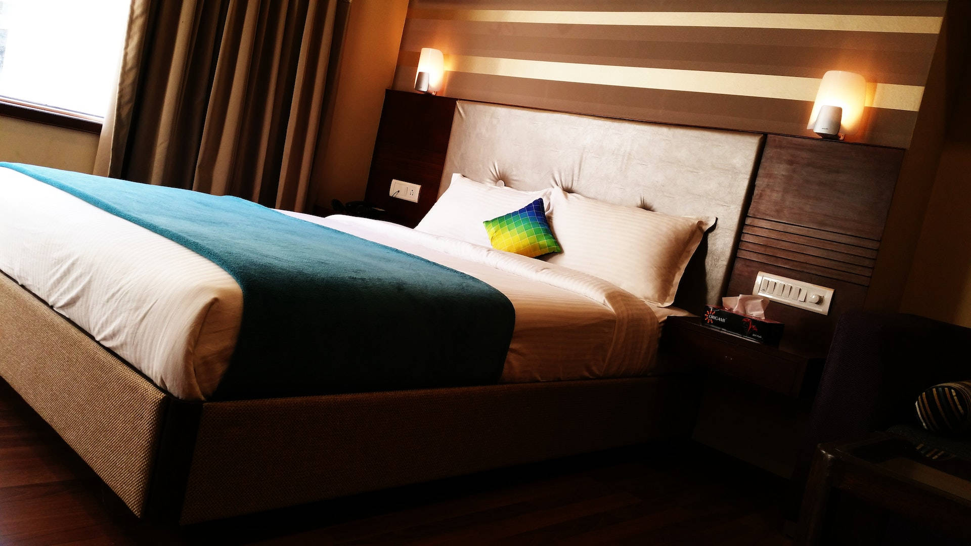bed 桌布 壁紙 — 舒適的飯店臥室，床鋪整齊，配有青綠色床罩和彩色枕頭，在溫暖的環境燈光下。