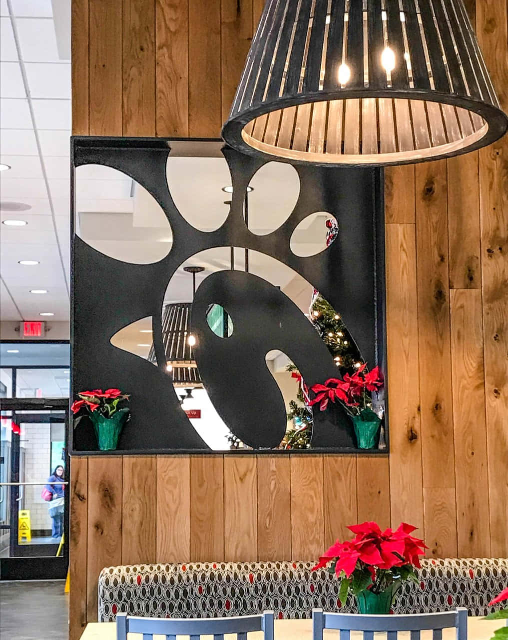 Chick Fil A 桌布 壁紙 — 舒適的餐廳內部，木質牆板上有一個大型黑色爪印鏡子，由條形吊燈照明，並以紅色聖誕紅點綴。
