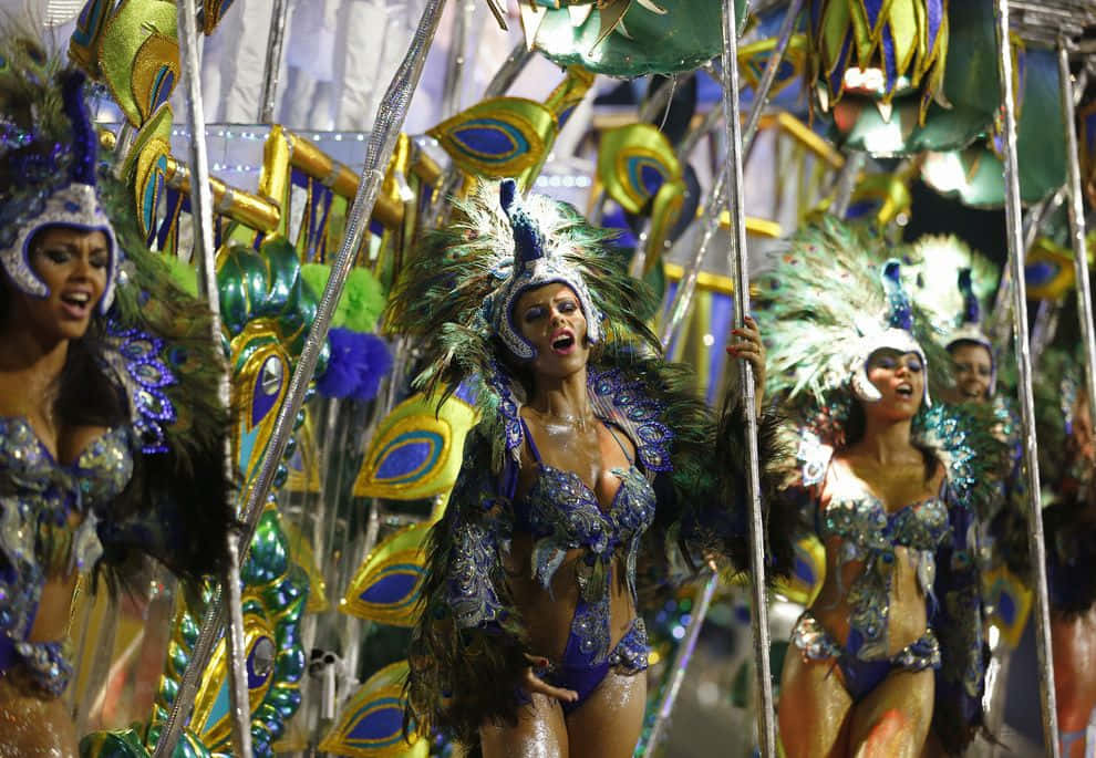Carnival 桌布 壁紙 — 舞者身穿耀眼的藍色、金色和綠色羽毛服裝，在明亮的嘉年華燈光下充滿活力地表演。