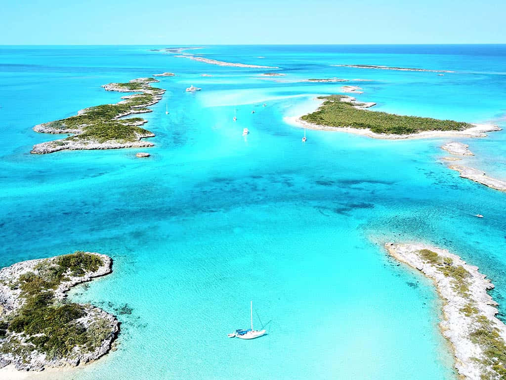 Bahamas Island 桌布 壁紙 — 航拍視角，碧綠松石色的海水蜿蜒於鬱鬱蔥蔥的綠色小島之間，帆船在清澈的藍天下悠然漂浮。