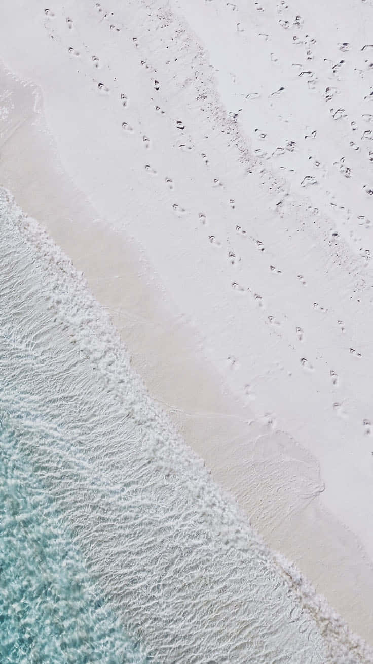 Cute Beach iPhone 桌布 壁紙 — 航拍視角，碧綠海浪輕拍純白沙灘，沙灘上散落著腳印。