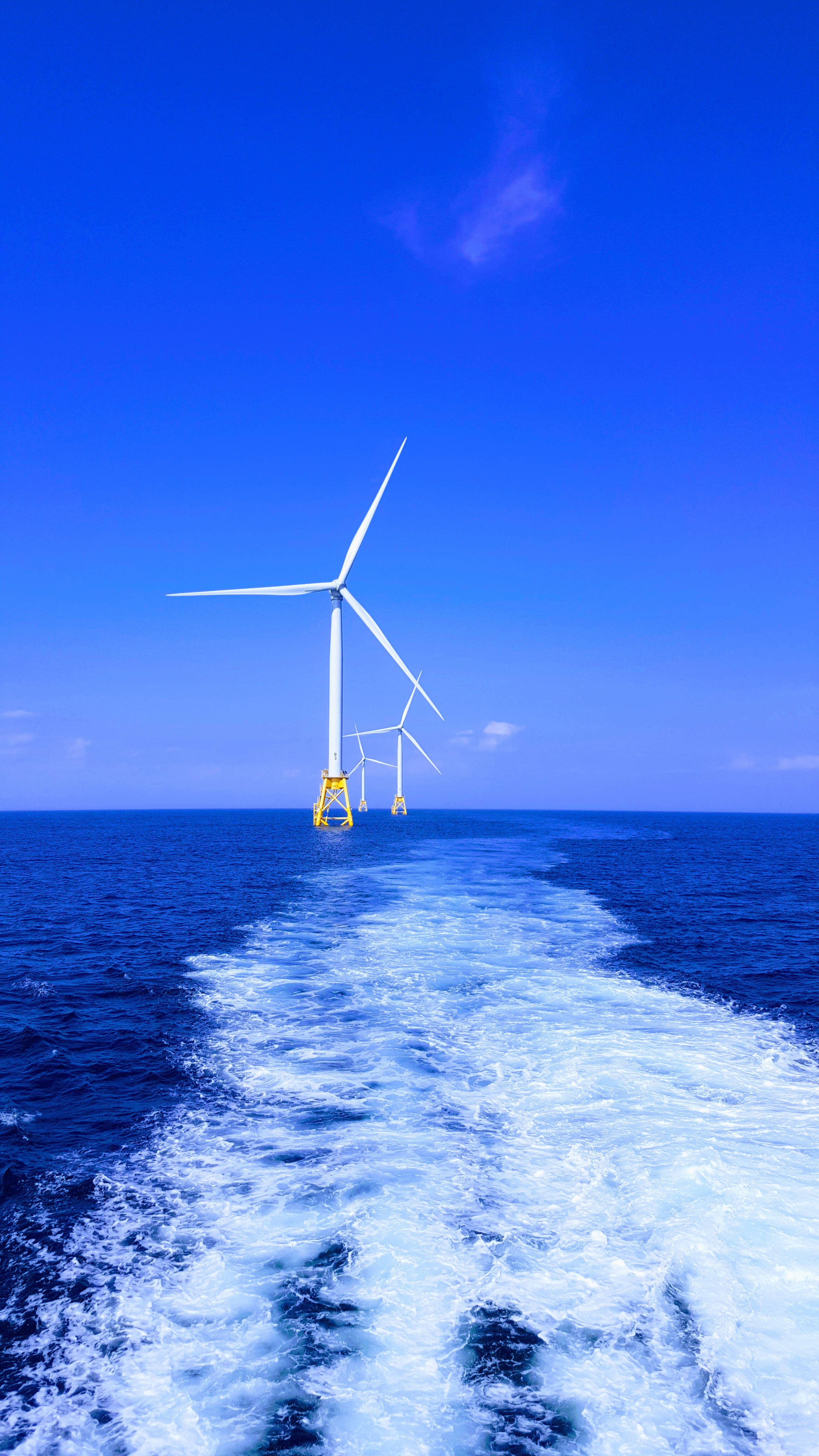 Energy 桌布 壁紙 — 船隻的尾流在清澈的藍天下引向高聳的海上風力發電機。