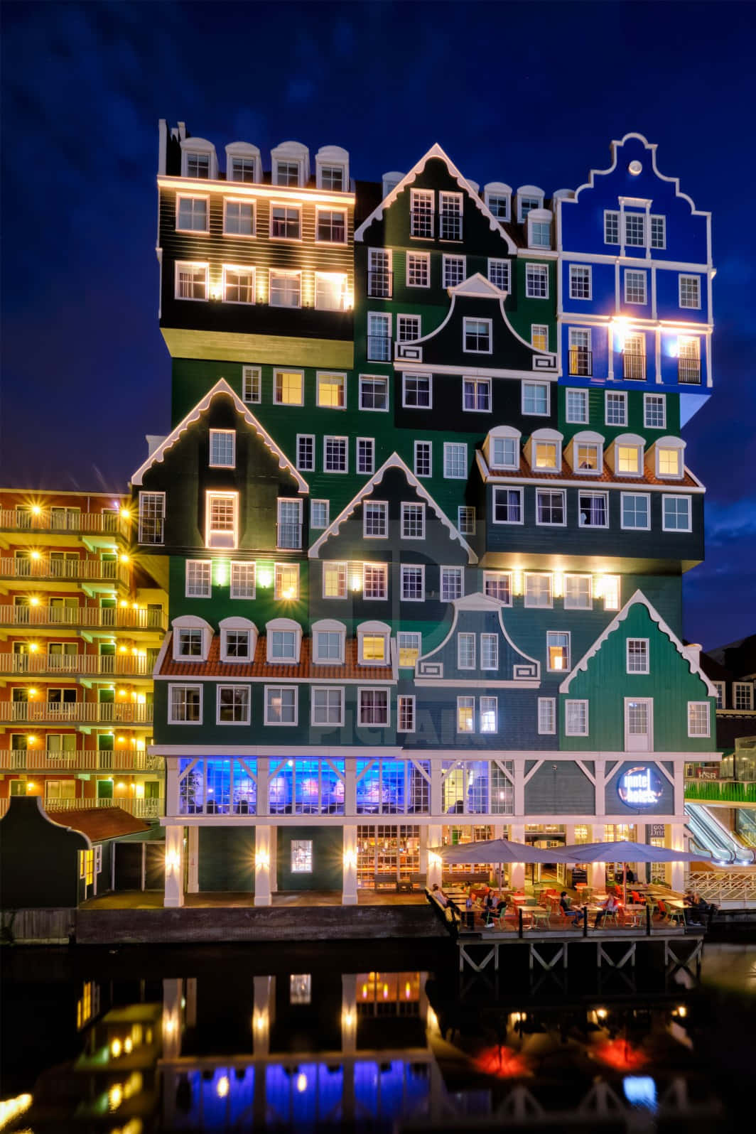 Building 桌布 壁紙 — 色彩繽紛、層疊的荷蘭風格建築在夜晚的活力景觀，發光的窗戶倒映在平靜的水面上。