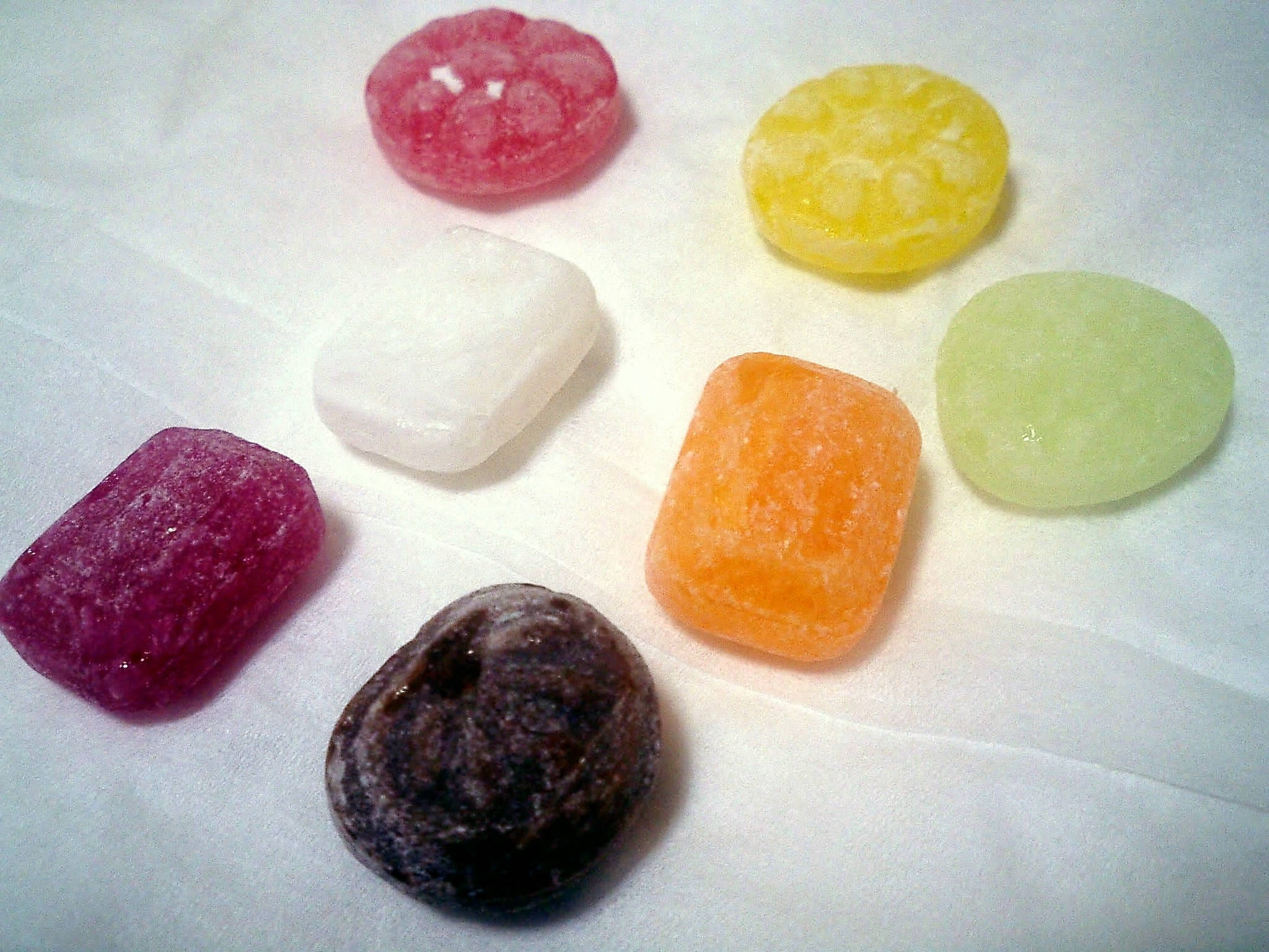 chewy 桌布 壁紙 — 色彩繽紛、形狀各異的糖衣糖果放在白色紙張表面上。