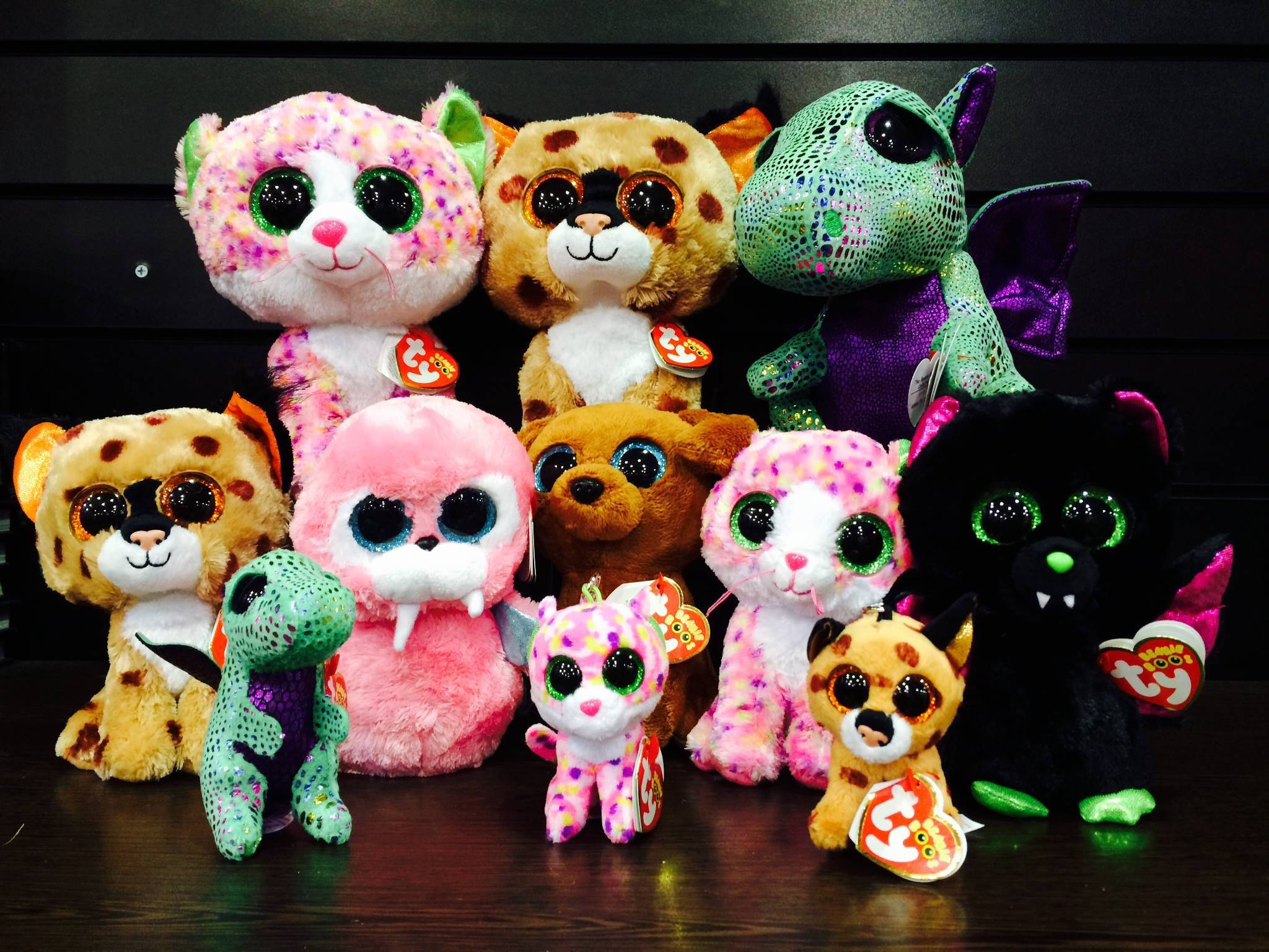 Beanie 桌布 壁紙 — 色彩繽紛的 Ty Beanie Boo 毛絨玩具系列，帶有閃爍眼睛和各種圖案，排列在深色木質表面上。
