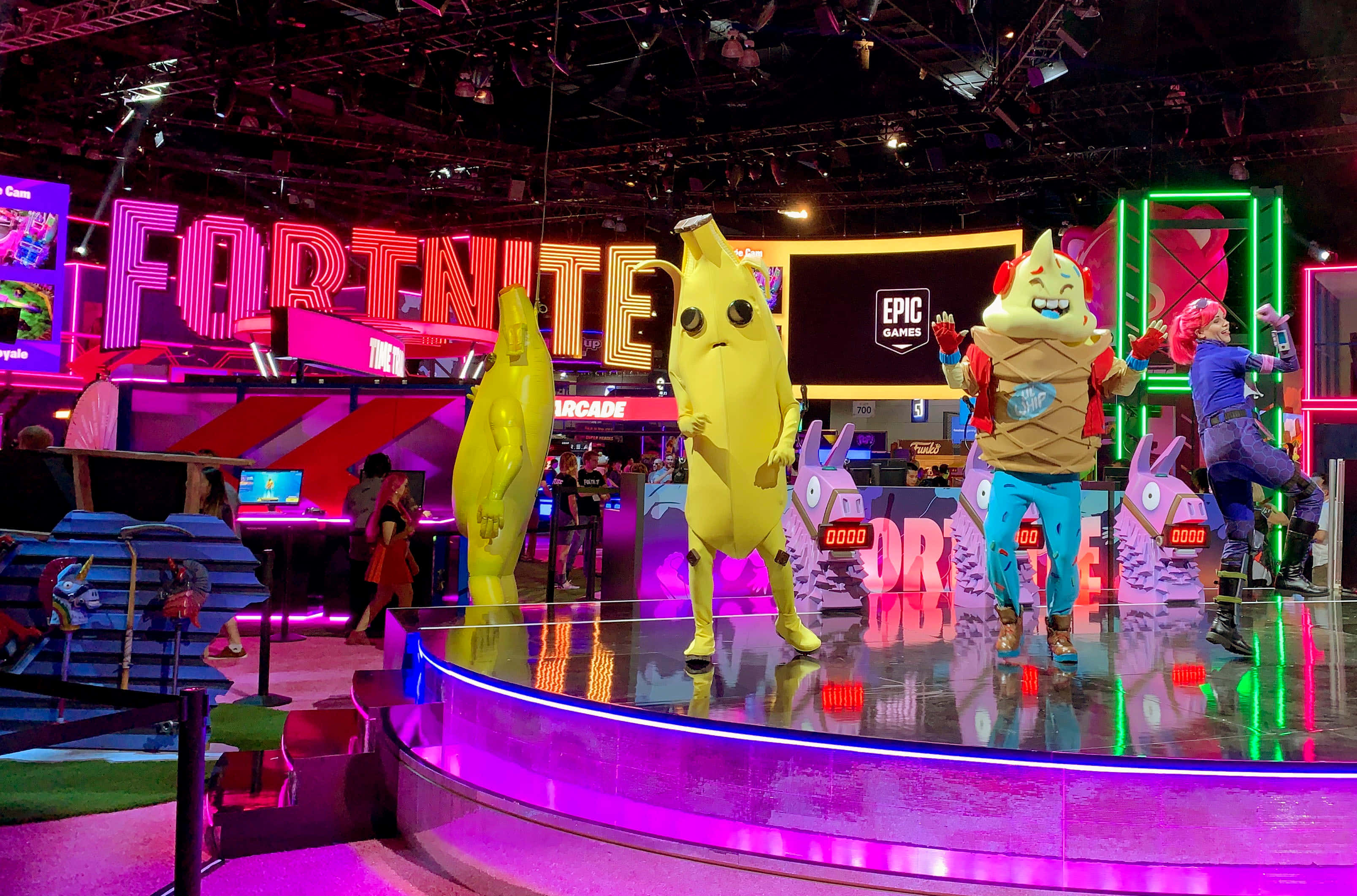 Gaming Conventions 桌布 壁紙 — 色彩繽紛的《要塞英雄》角色穿著香蕉和冰淇淋服裝，在 Epic Games 活動的霓虹燈舞台上表演。