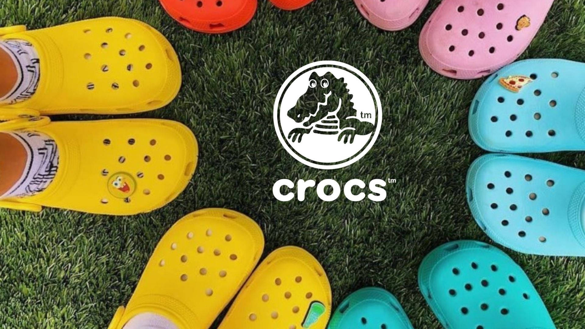 Crocs 桌布 壁紙 — 色彩繽紛的Crocs涼鞋在綠色草地上圍繞Crocs標誌排列成圓圈。