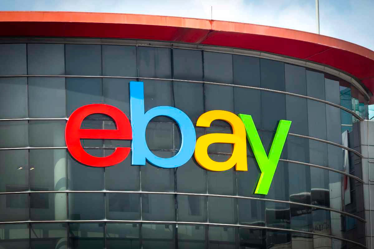 品牌 桌布 壁紙 — 色彩繽紛的eBay標誌，以粗體紅、藍、黃、綠色字母組成，安裝在現代玻璃建築外牆上，天空部分多雲。