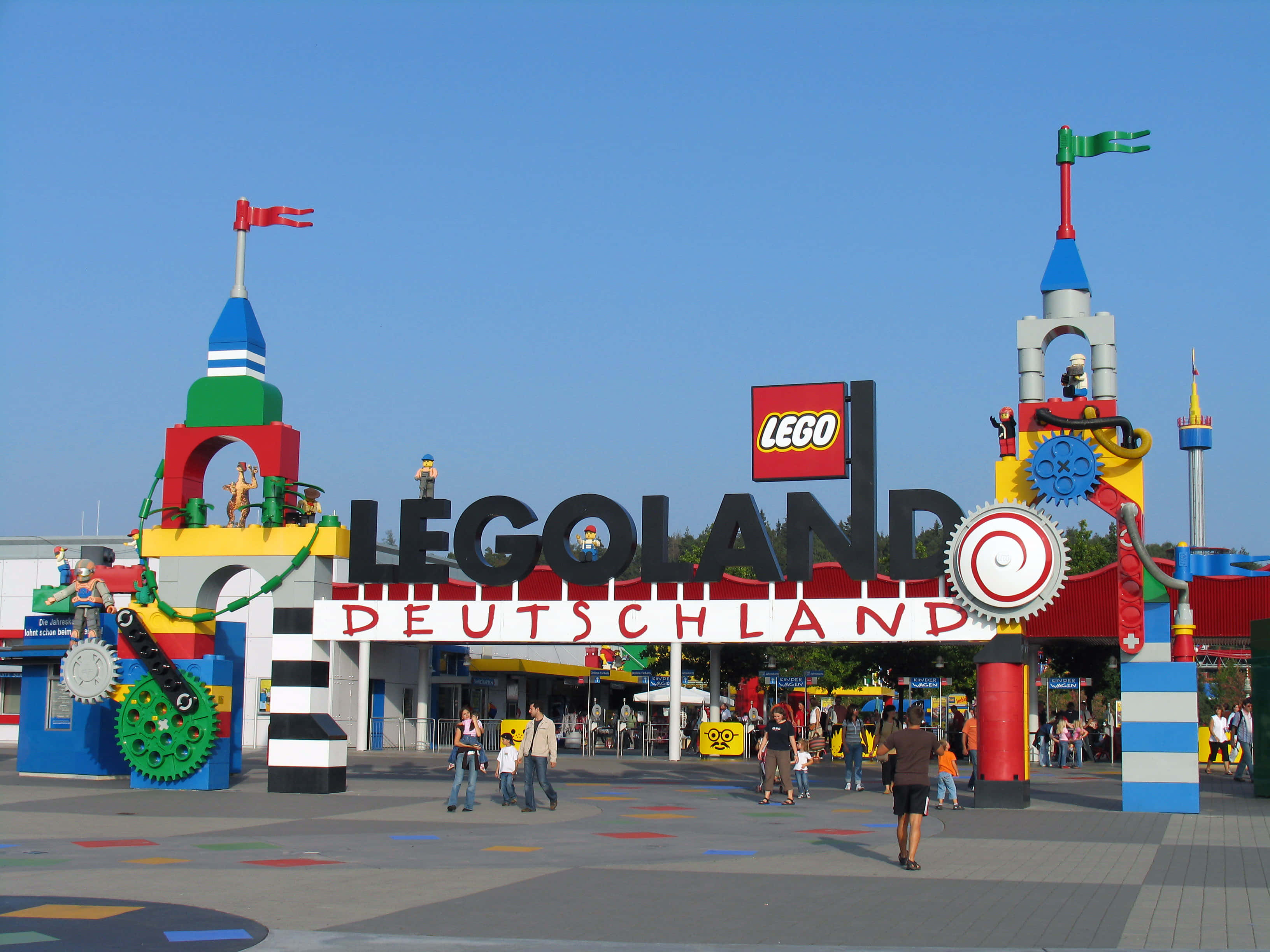 Legoland 桌布 壁紙 — 色彩繽紛的LEGO主題入口，通往LEGOLAND Deutschland，擁有彩色積木塔、齒輪和遊客，在晴朗藍天下。