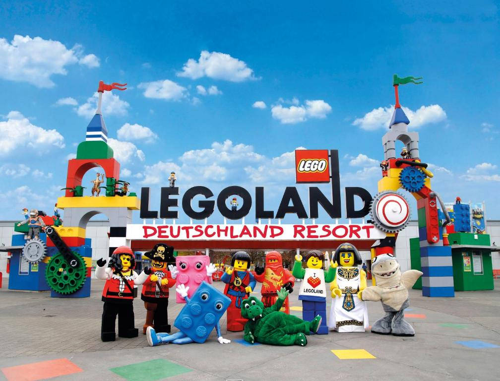 樂高 桌布 壁紙 — 色彩繽紛的LEGO角色在晴朗的藍天下，於充滿活力的LEGOLAND Deutschland Resort入口前愉快地擺姿勢。