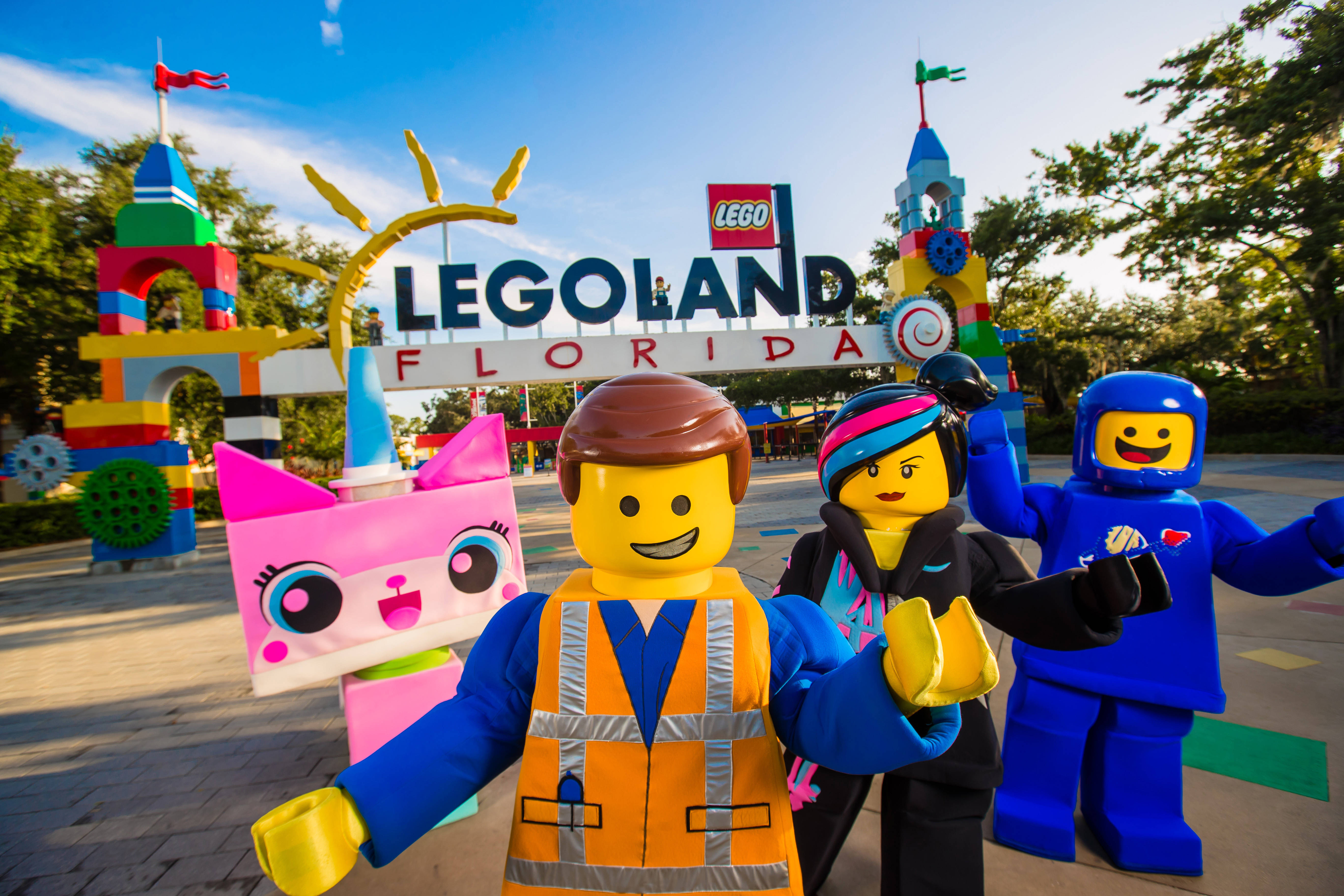樂高 桌布 壁紙 — 色彩繽紛的LEGO角色在晴朗藍天下，於色彩繽紛的LEGOLAND Florida入口愉快地擺姿勢。