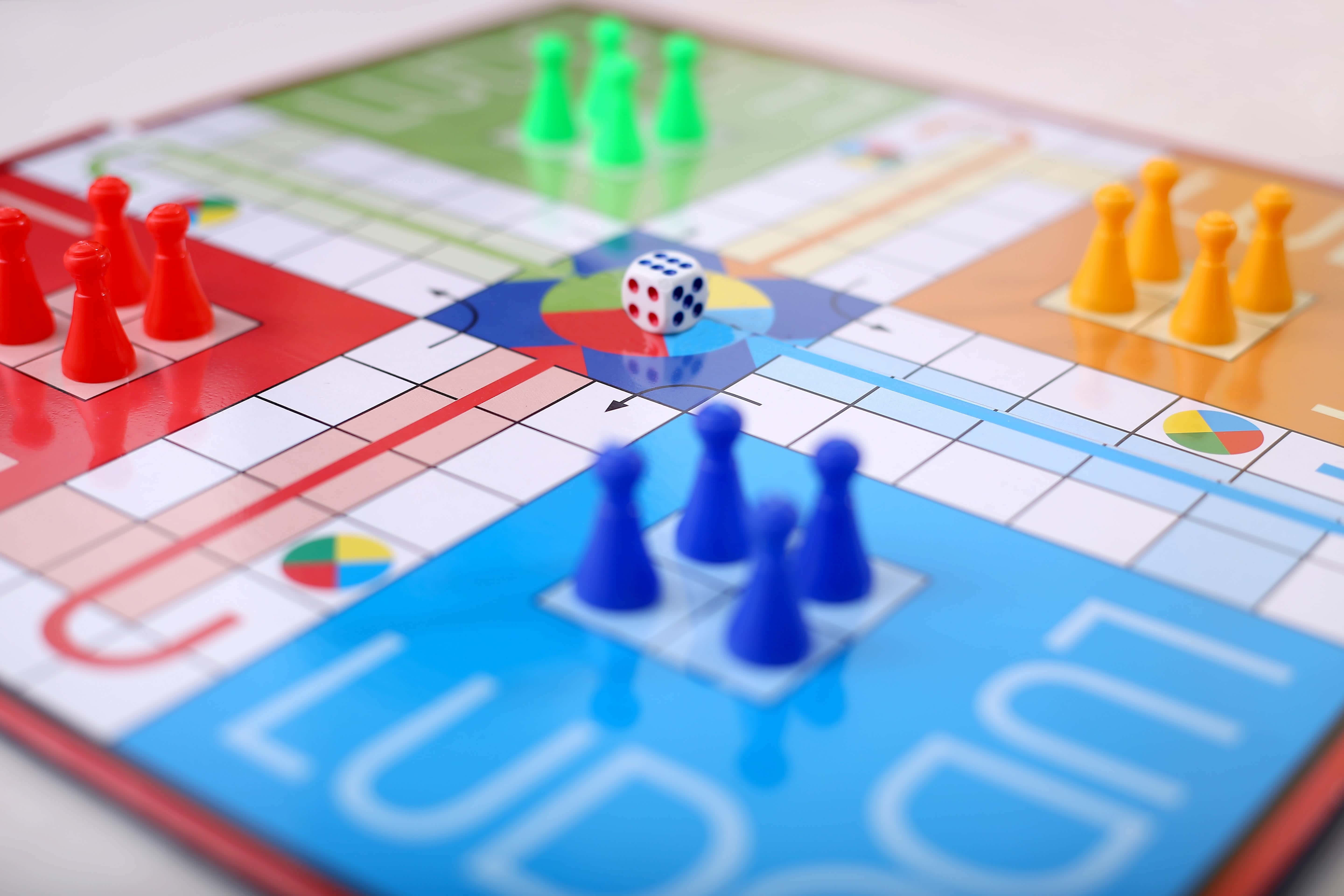 Educational Games 桌布 壁紙 — 色彩繽紛的Ludo棋盤遊戲特寫，有紅色、藍色和綠色的棋子，以及一個放在中央圓圈上的白色骰子。