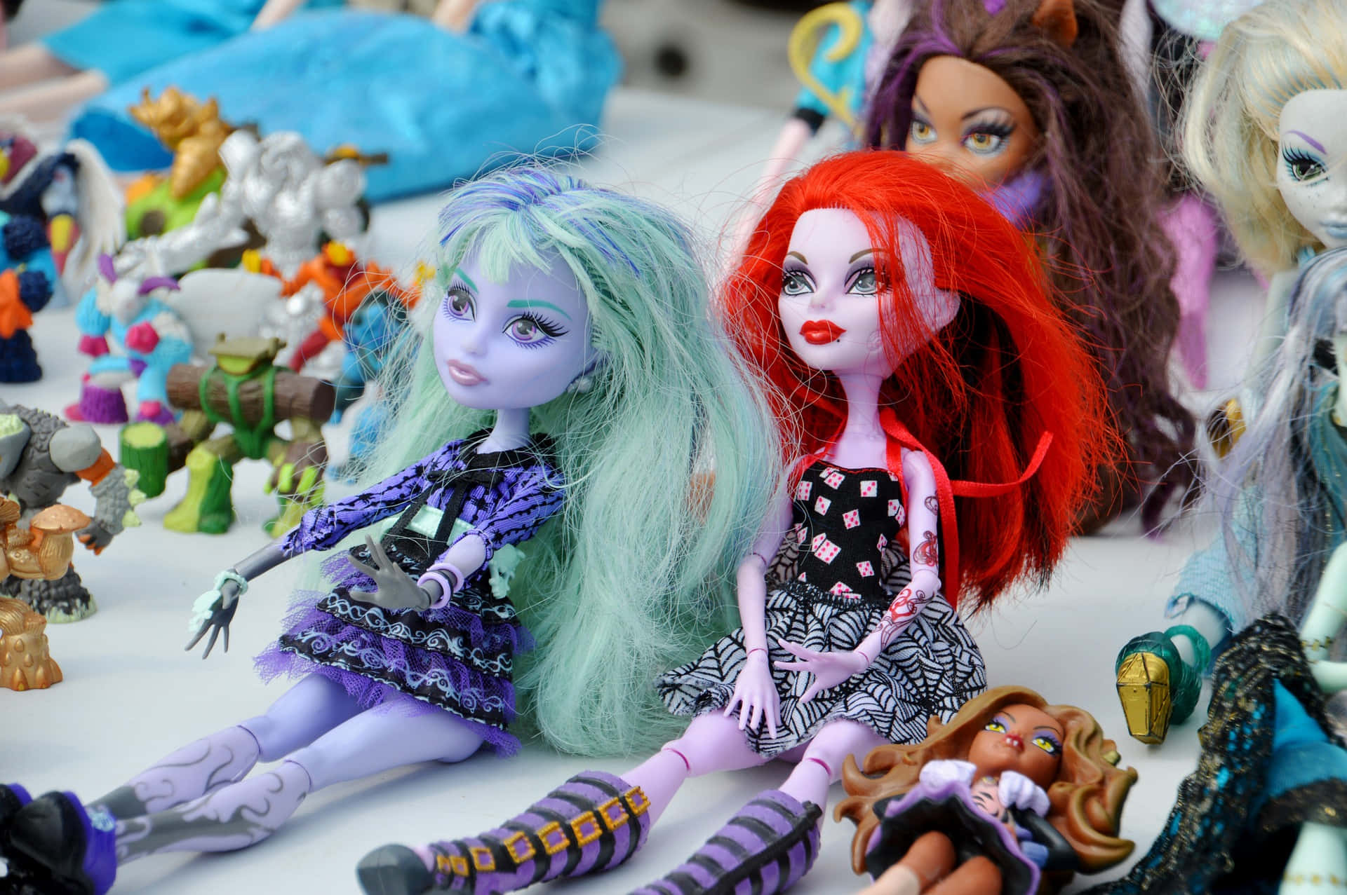 Monster High 桌布 壁紙 — 色彩繽紛的Monster High公仔，擁有彩色頭髮和哥德式服裝，坐在白色表面上的各種動作公仔之間。