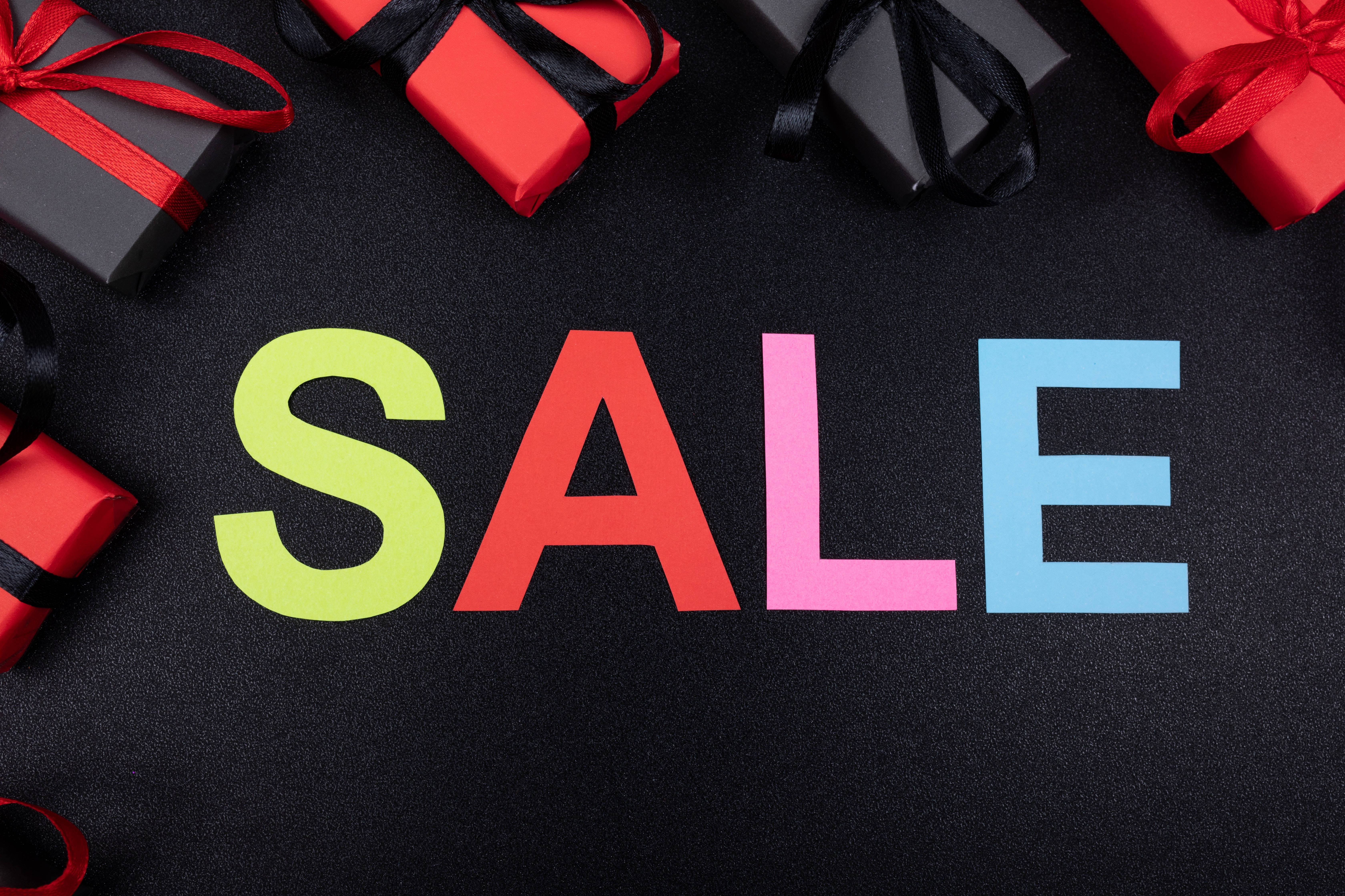 Sales 桌布 壁紙 — 色彩繽紛的SALE字母，被紅色和黑色禮物盒包圍，置於深色紋理表面上。