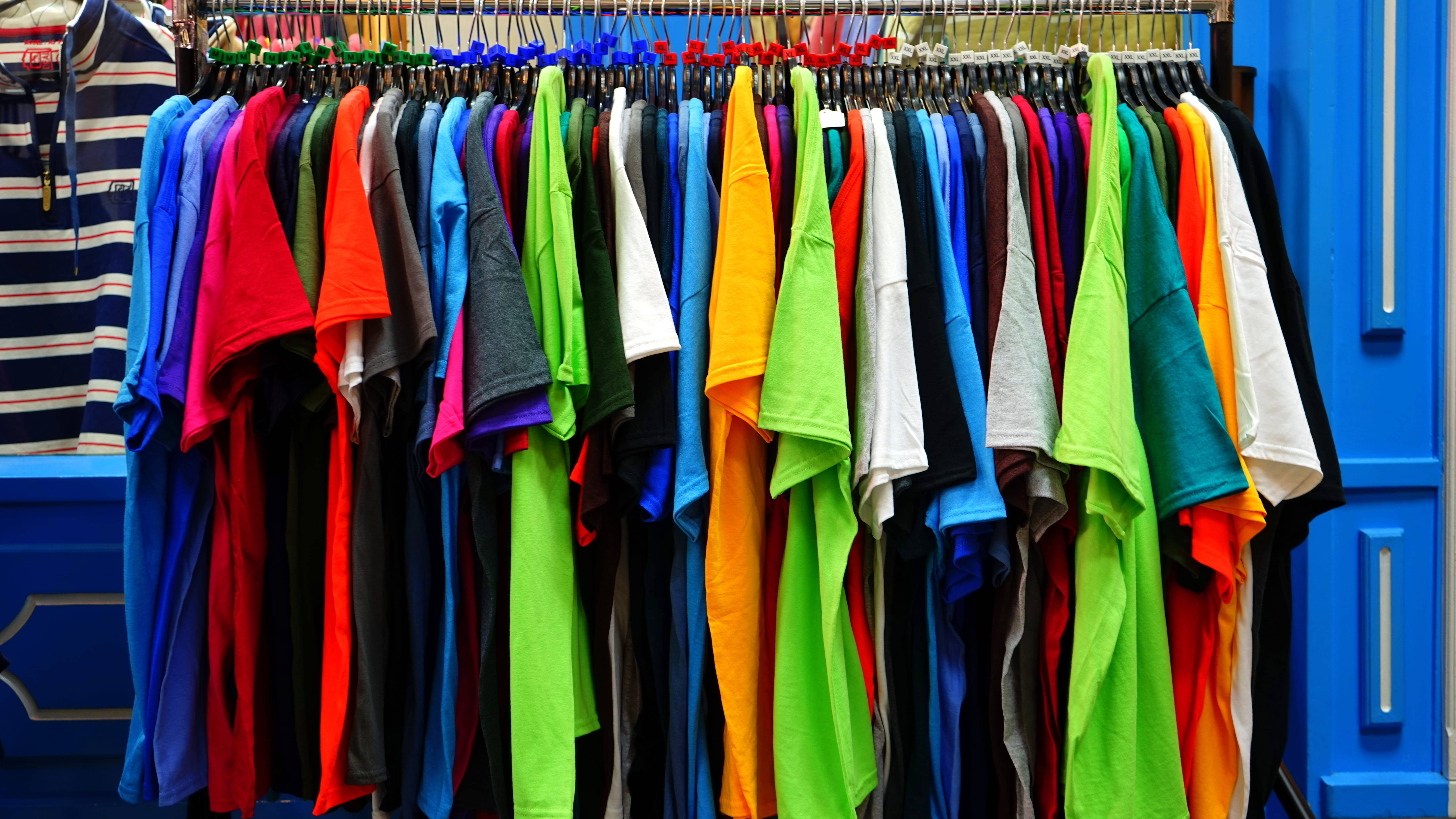 Clothes 桌布 壁紙 — 色彩繽紛的T恤整齊地掛在金屬架上，背景是鮮明的藍色牆壁。