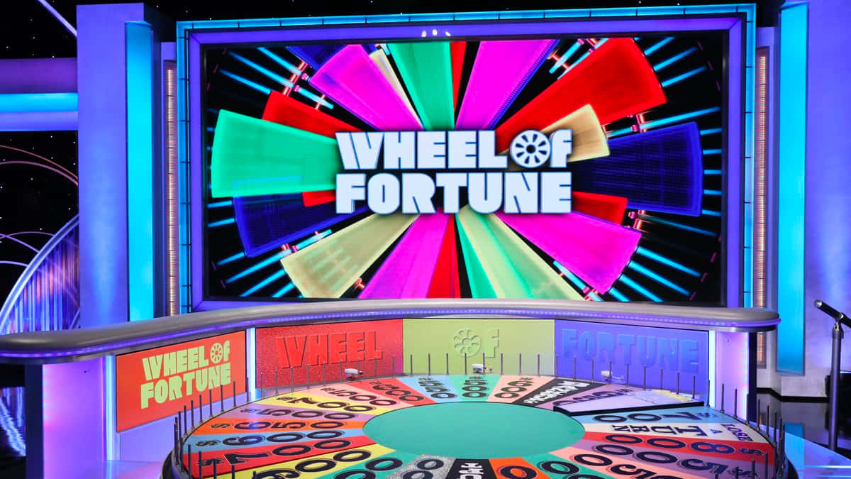 game 桌布 壁紙 — 色彩繽紛的Wheel of Fortune遊戲節目場景，配有旋轉輪盤和閃爍的舞台燈光。