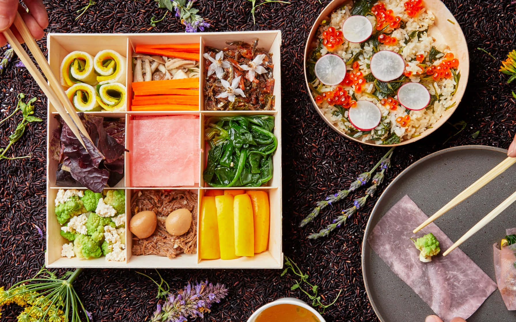 Food Table 桌布 壁紙 — 色彩繽紛的便當盒俯視圖，整齊排列著壽司卷、紅蘿蔔、肉類、蔬菜和雞蛋，周圍環繞著薰衣草和黑米。