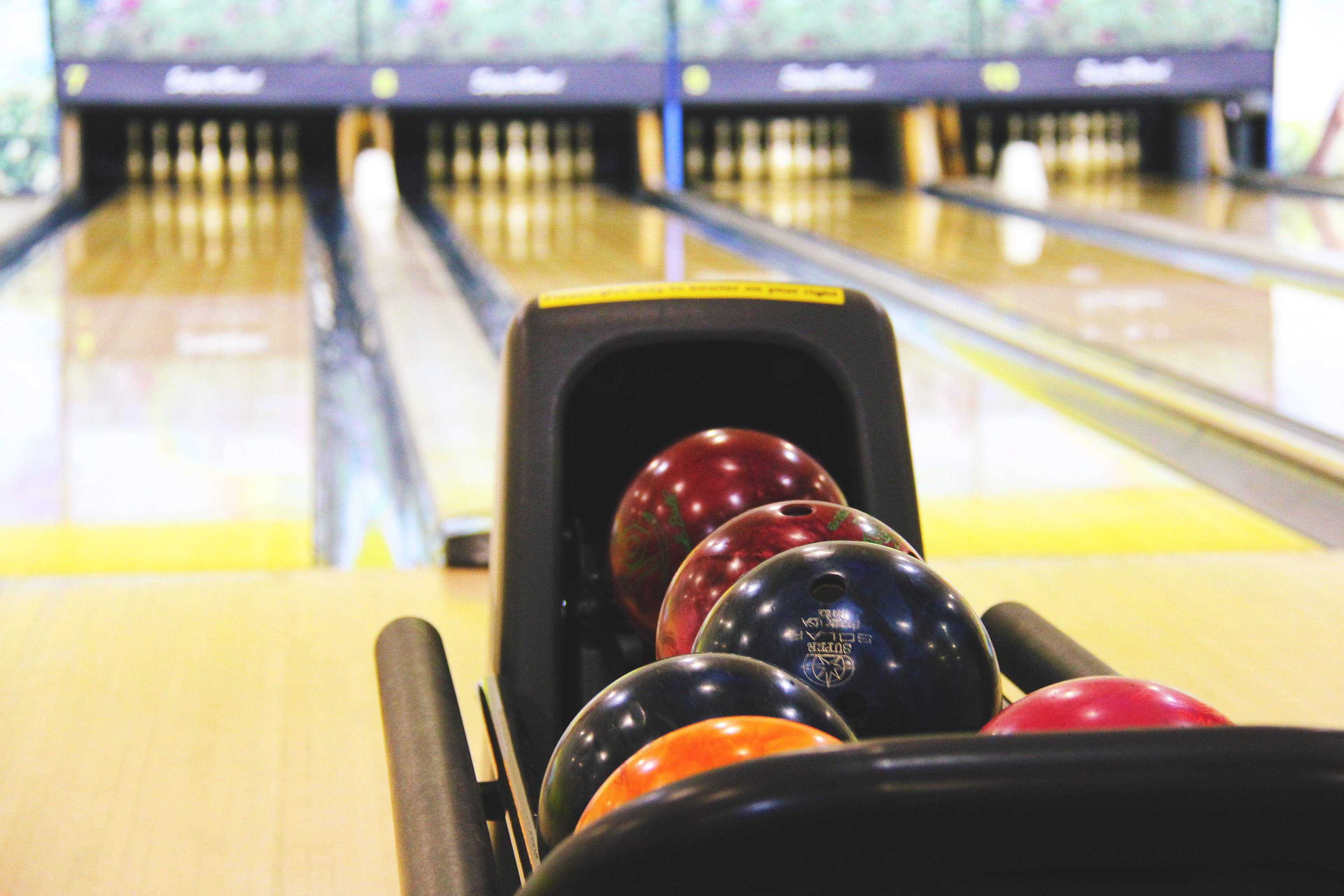 Bowling 桌布 壁紙 — 色彩繽紛的保齡球放在球架上，背景中的球道和球瓶模糊不清的近距離視角。