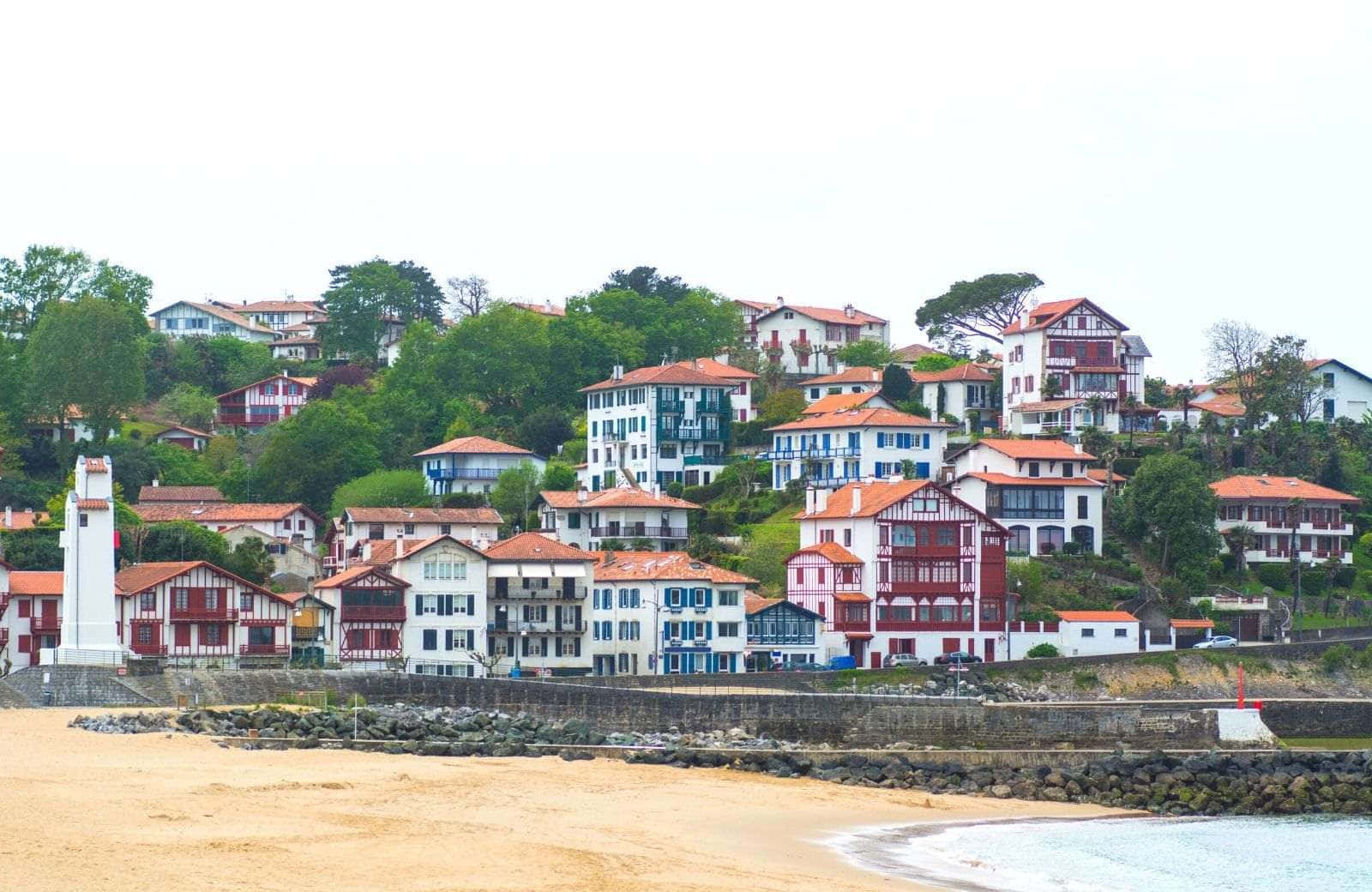 French Beach 桌布 壁紙 — 色彩繽紛的傳統房屋，紅瓦白牆，沿著沙灘和寧靜大海旁的綠色山坡層疊而下。