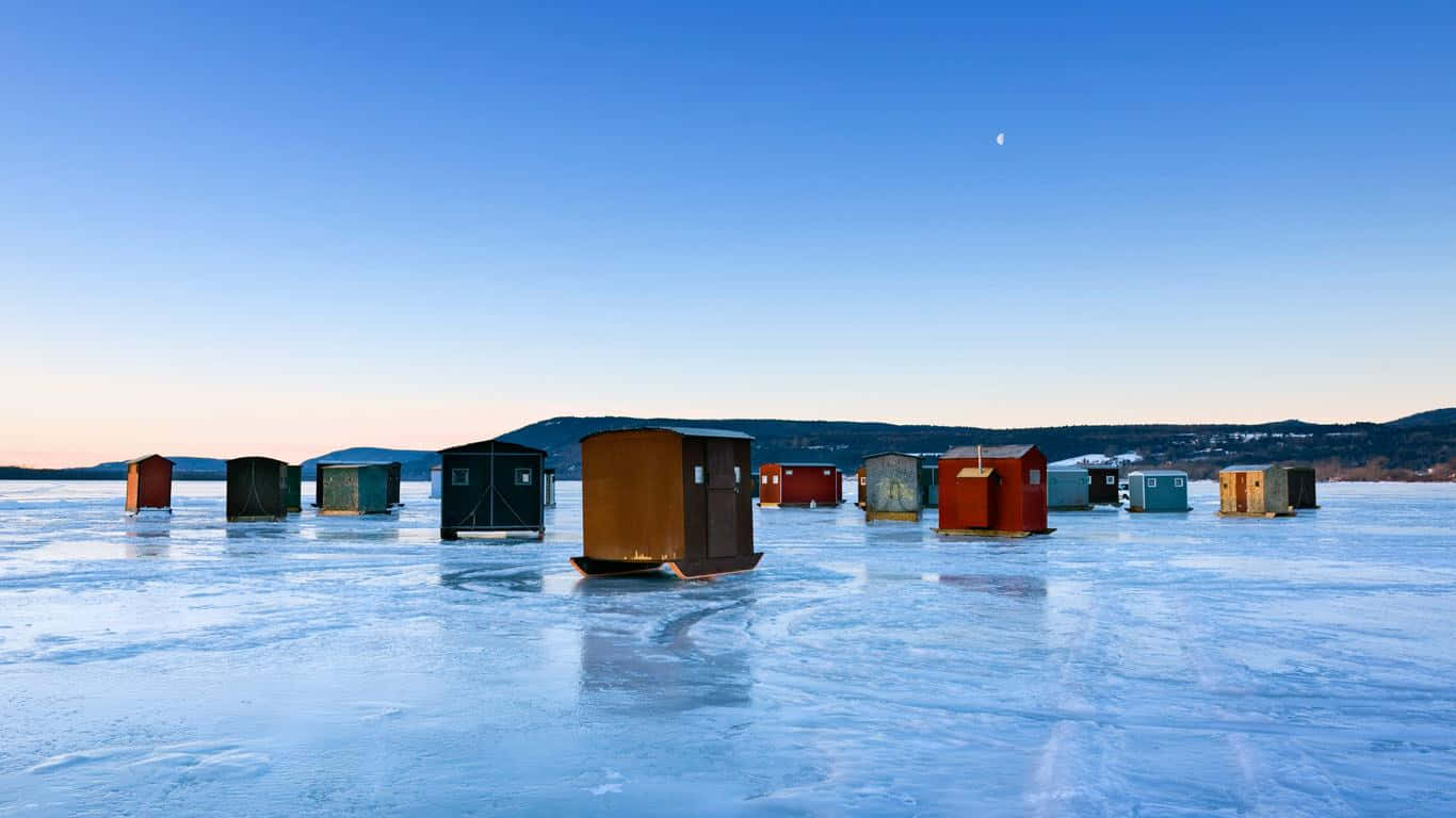 Ice Fishing 桌布 壁紙 — 色彩繽紛的冰釣小屋點綴在廣闊的冰凍湖面上，天空清澈湛藍，掛著一彎新月。