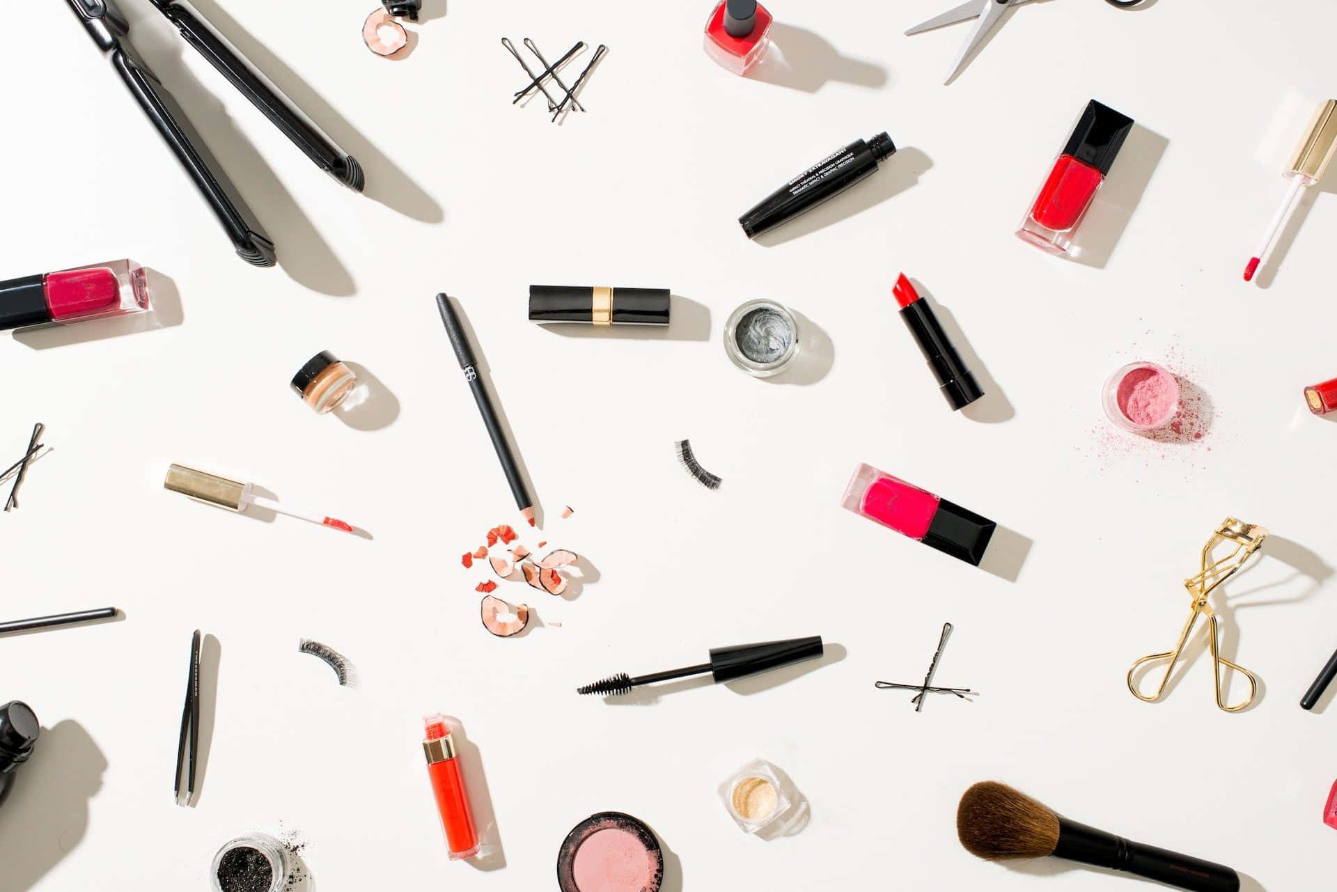 Mac Cosmetics 桌布 壁紙 — 色彩繽紛的化妝品和美容工具散落在明亮的白色表面上，帶有強烈陰影的平鋪佈局。