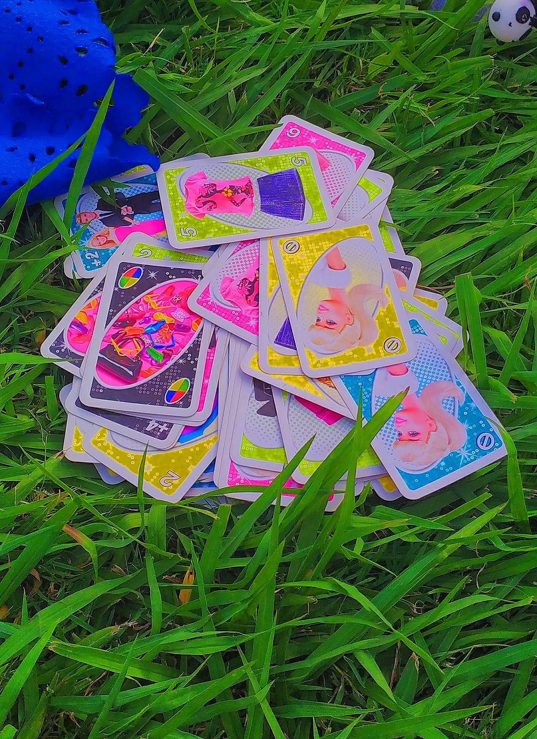 Uno 桌布 壁紙 — 色彩繽紛的卡通卡片散落在茂盛的綠色草地上，附近有一個藍色毛絨玩具。