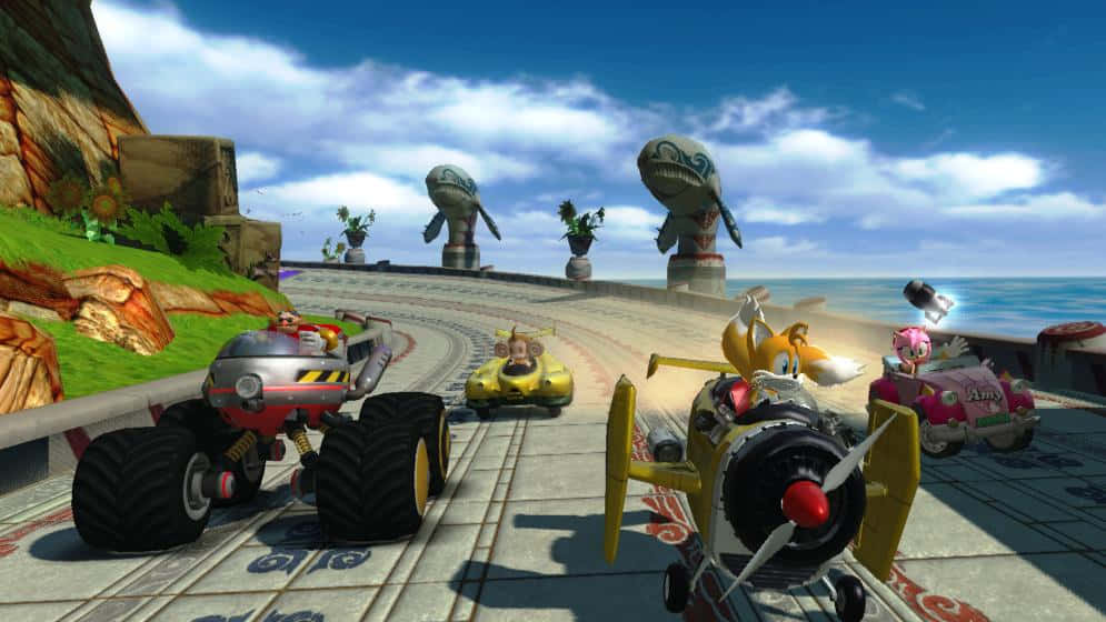 Sonic And All-stars Racing Transformed 桌布 壁紙 — 色彩繽紛的卡通賽車沿著海岸賽道奔馳，賽道上有巨大的石頭頭像和海洋景觀，天空湛藍明亮。