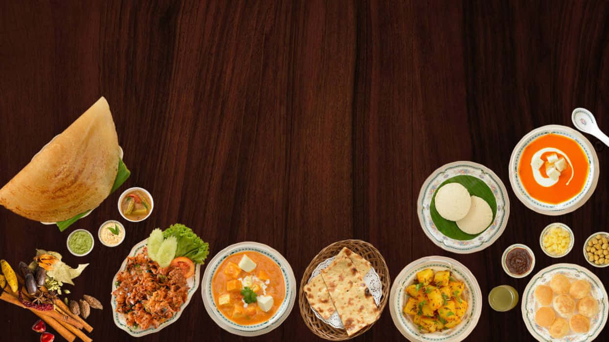 Indian Food 桌布 壁紙 — 色彩繽紛的印度菜餚，包括多薩、薩摩薩和咖哩，擺放在深色木桌上。