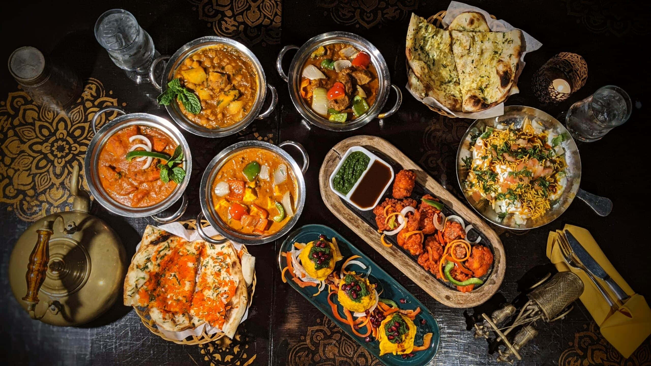 Indian 桌布 壁紙 — 色彩繽紛的印度菜餚以金屬碗和木托盤盛裝，擺放在深色圖案桌上，盡顯奢華。