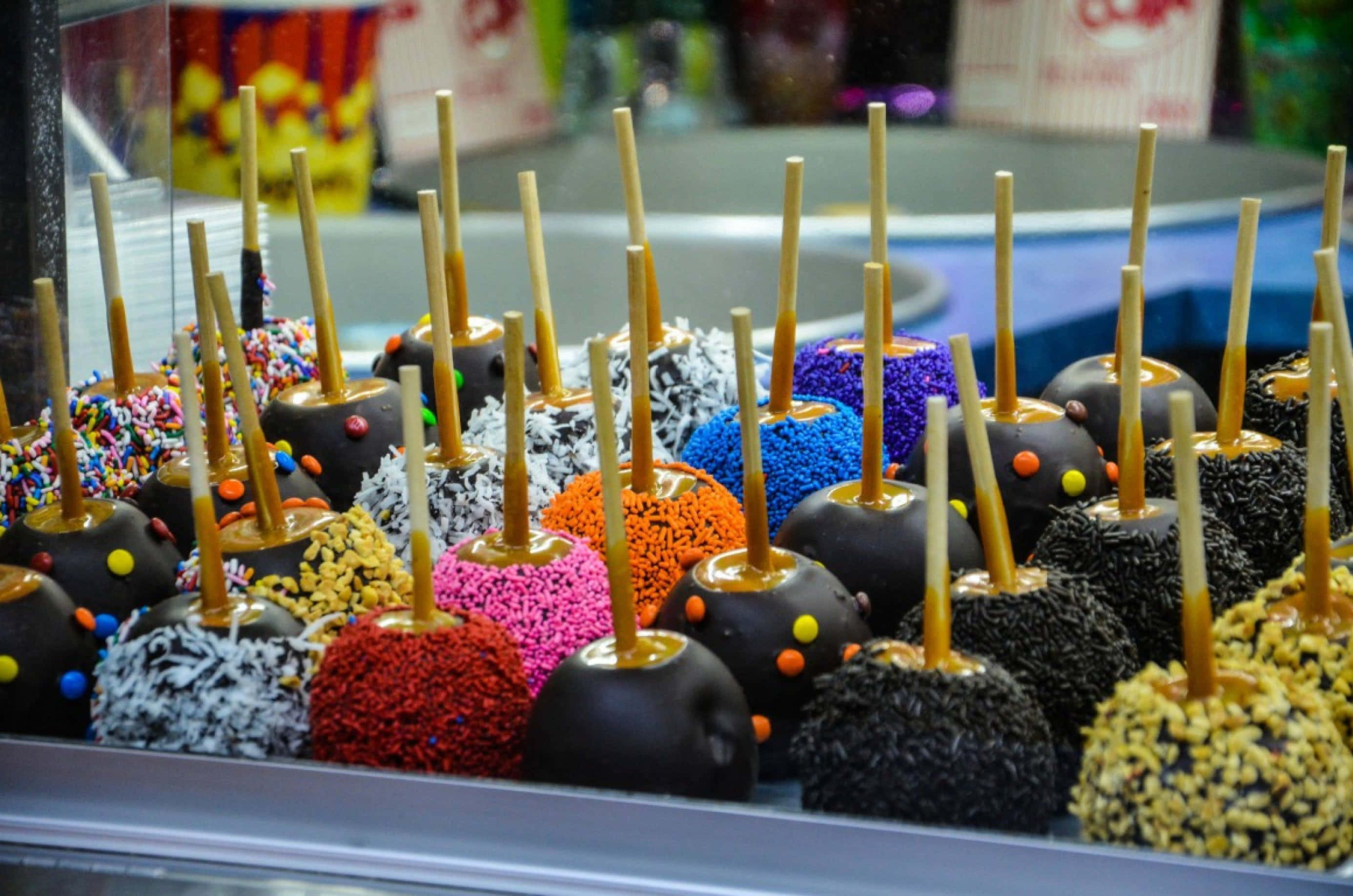 Candy Apples 桌布 壁紙 — 色彩繽紛的各式糖果蘋果，裹上彩色糖粒和配料，插在棒上展示。