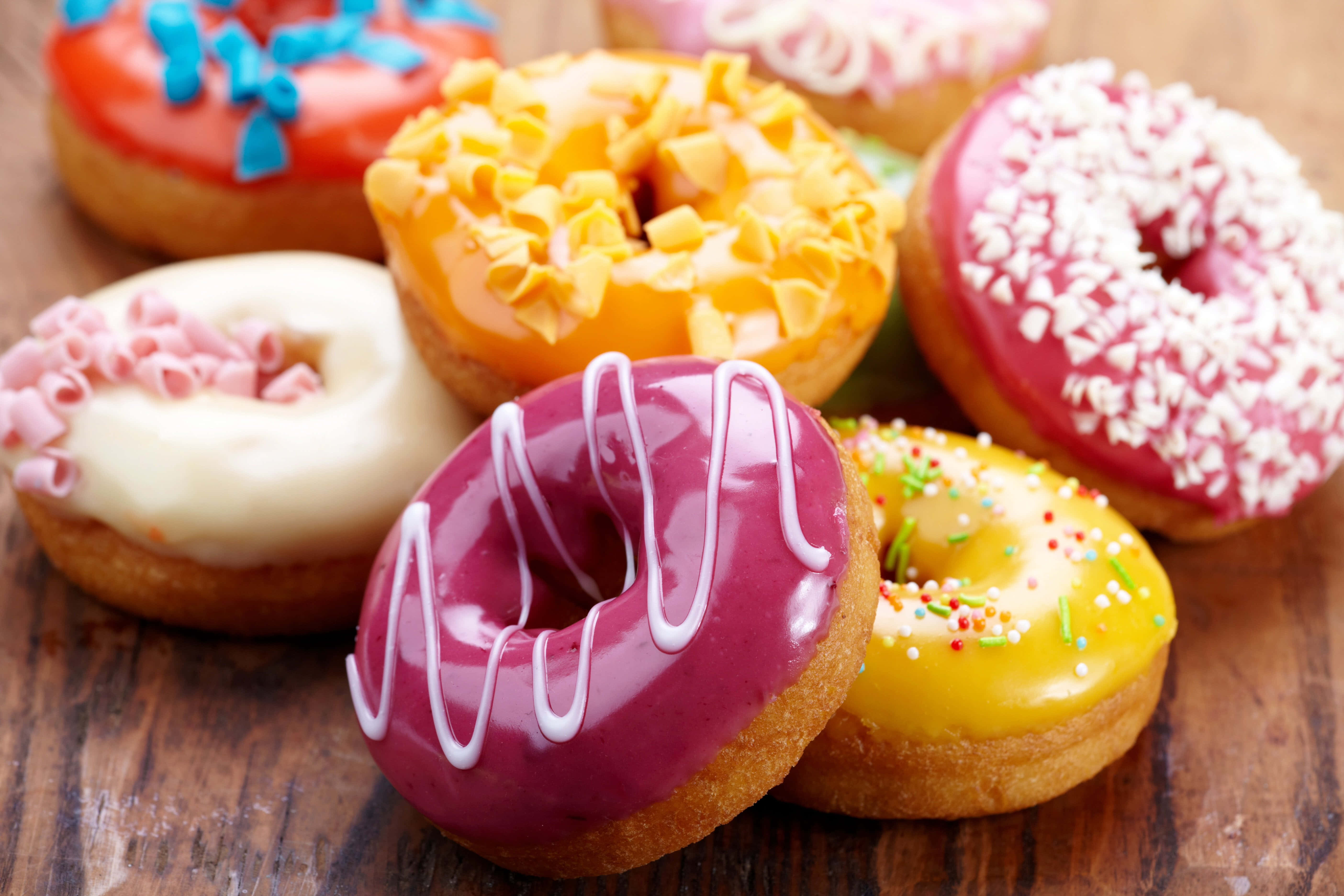 Donut 桌布 壁紙 — 色彩繽紛的各式釉面甜甜圈，搭配彩色配料，擺放在質樸的木質表面上，呈現鮮明的近距離特寫。