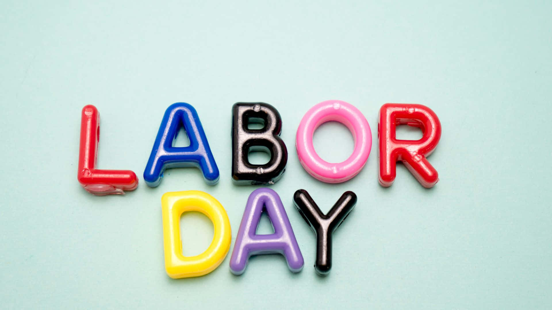 勞動節 桌布 壁紙 — 色彩繽紛的塑膠字母拼出 LABOR DAY，排列在柔和的薄荷綠色背景上。