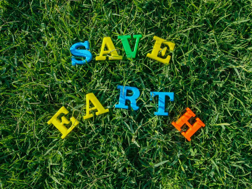 1024x768 桌布 壁紙 — 色彩繽紛的塑膠字母拼出「SAVE EARTH」，散落在陽光下鮮綠的草地上。