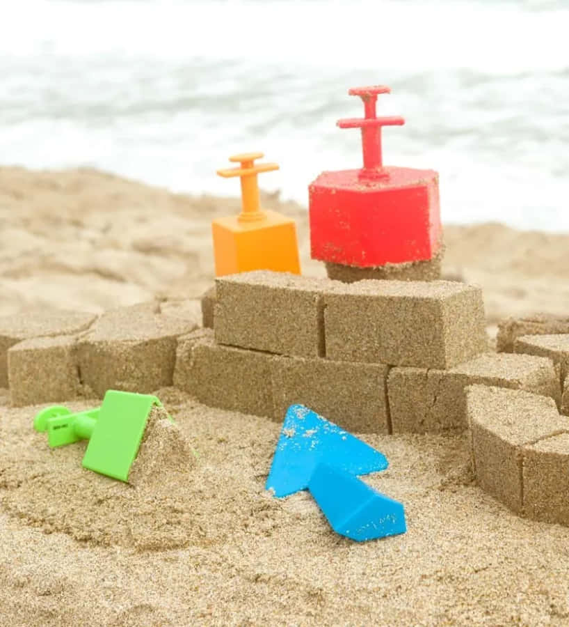 Beach Toys 桌布 壁紙 — 色彩繽紛的塑膠沙灘玩具圍繞著一個在海邊用模製積木建造的沙堡。