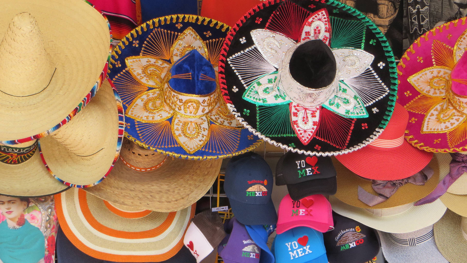 Mexican 桌布 壁紙 — 色彩繽紛的墨西哥闊邊帽和「yo mex」帽子在熱鬧的市場攤位中展示。