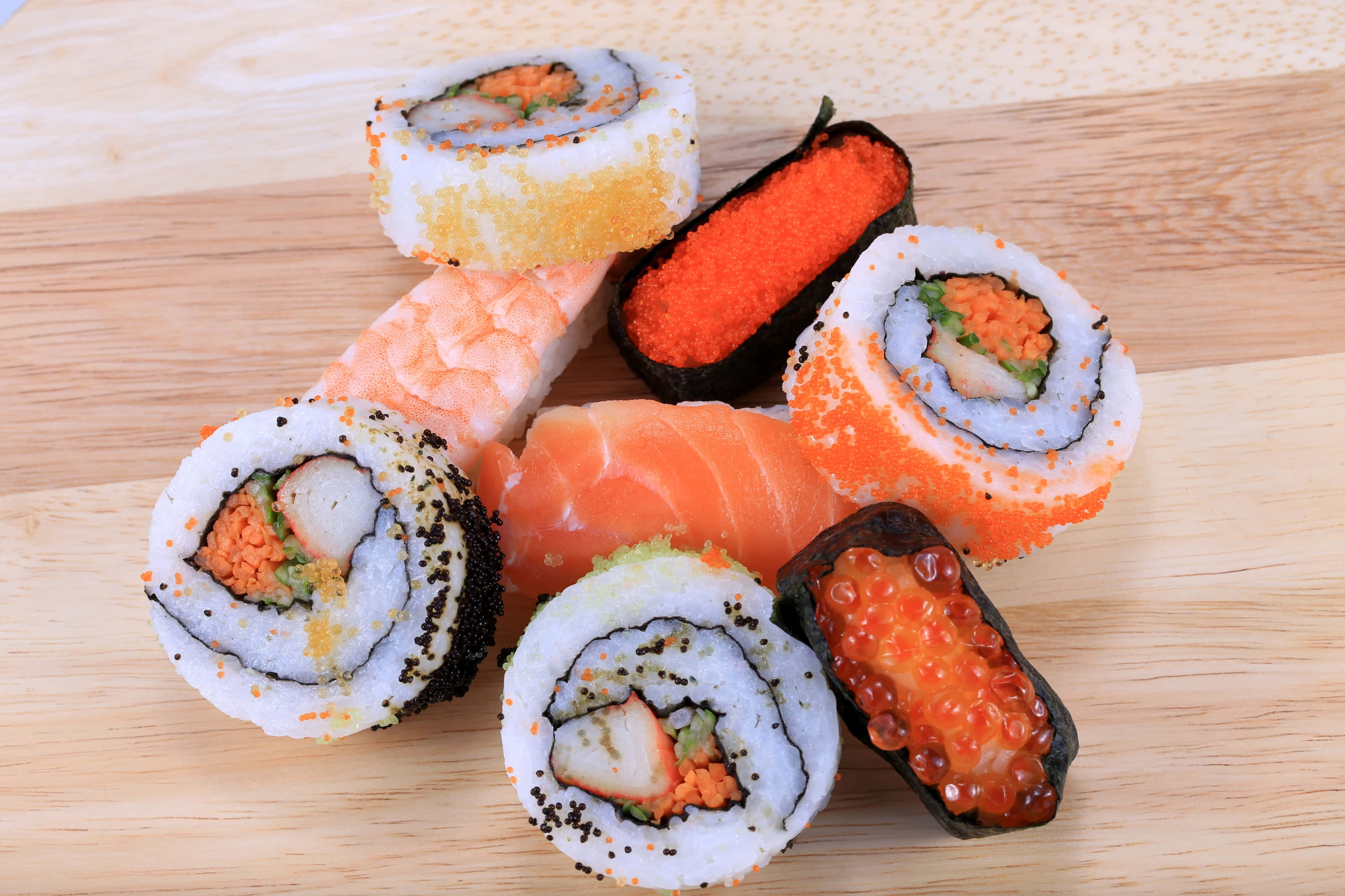 Sushi 桌布 壁紙 — 色彩繽紛的壽司卷和刺身擺放在一塊紋理清晰的淺色木板上。