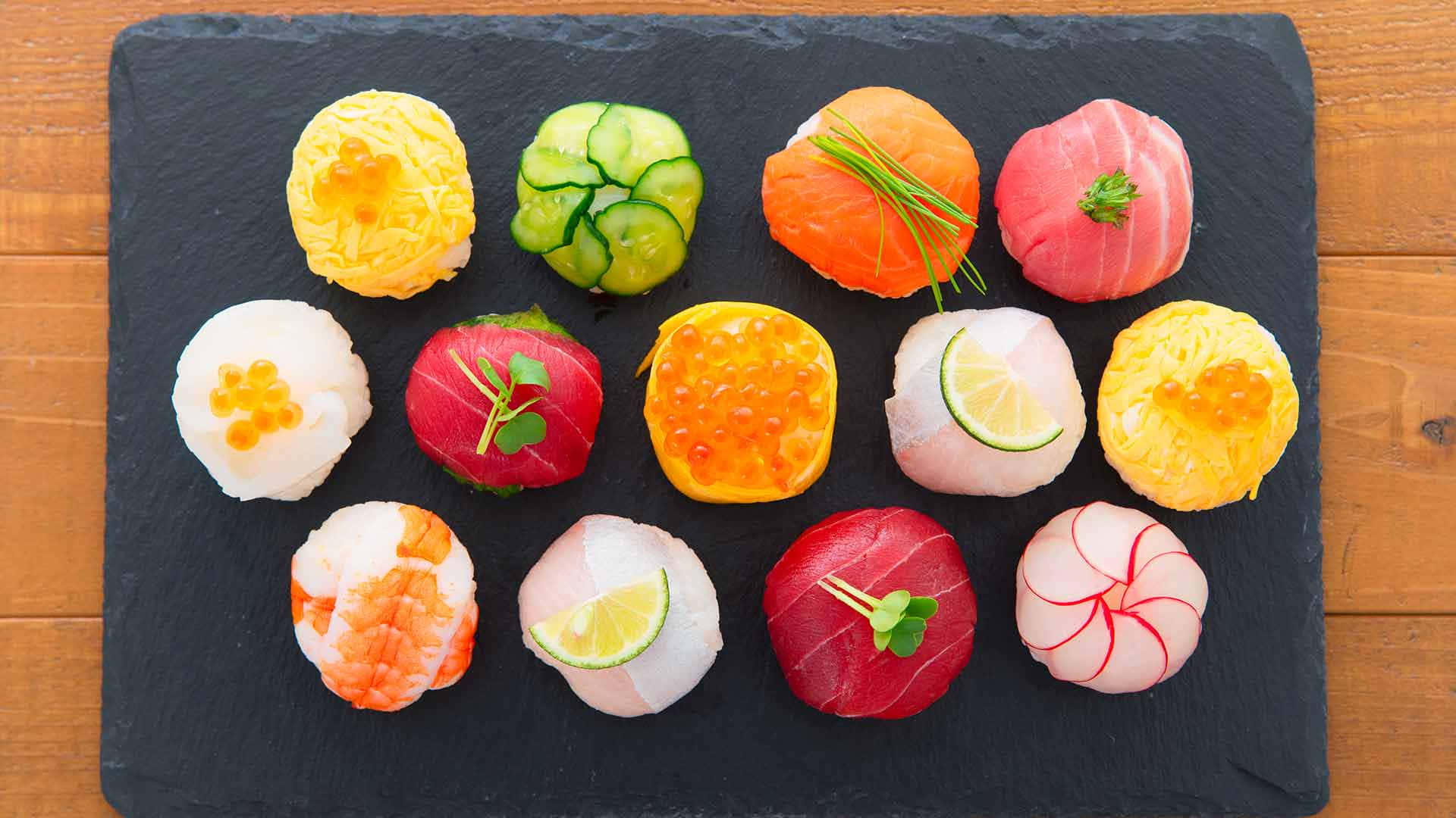 Food Photography 桌布 壁紙 — 色彩繽紛的壽司拼盤藝術地擺放在深色石板托盤上，置於溫暖的木桌上。