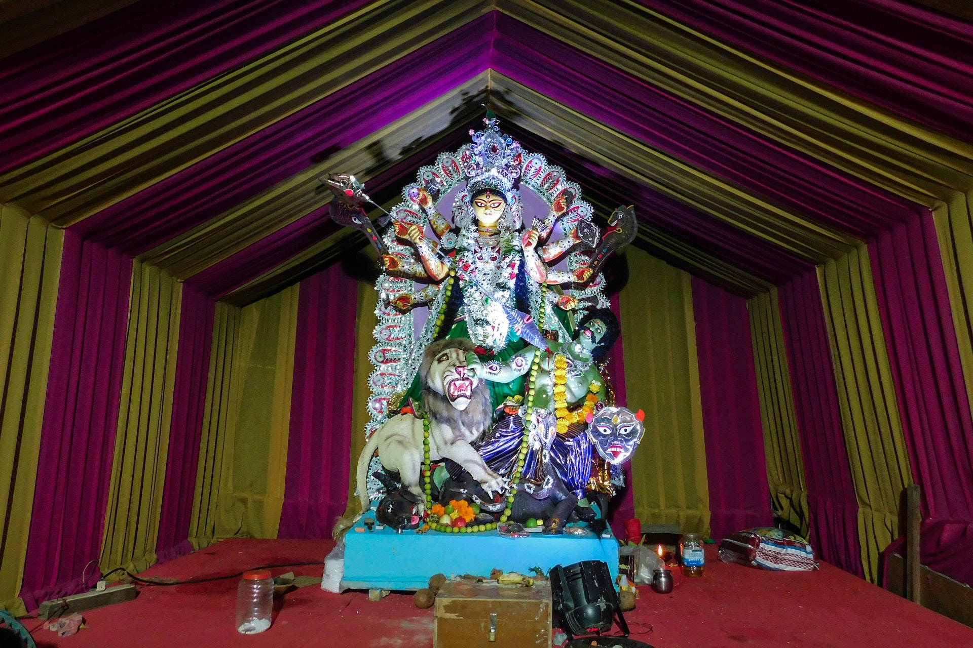 Durga 桌布 壁紙 — 色彩繽紛的多臂杜爾迦神像坐在獅子寶座上，下方是紫色和金色的垂簾。