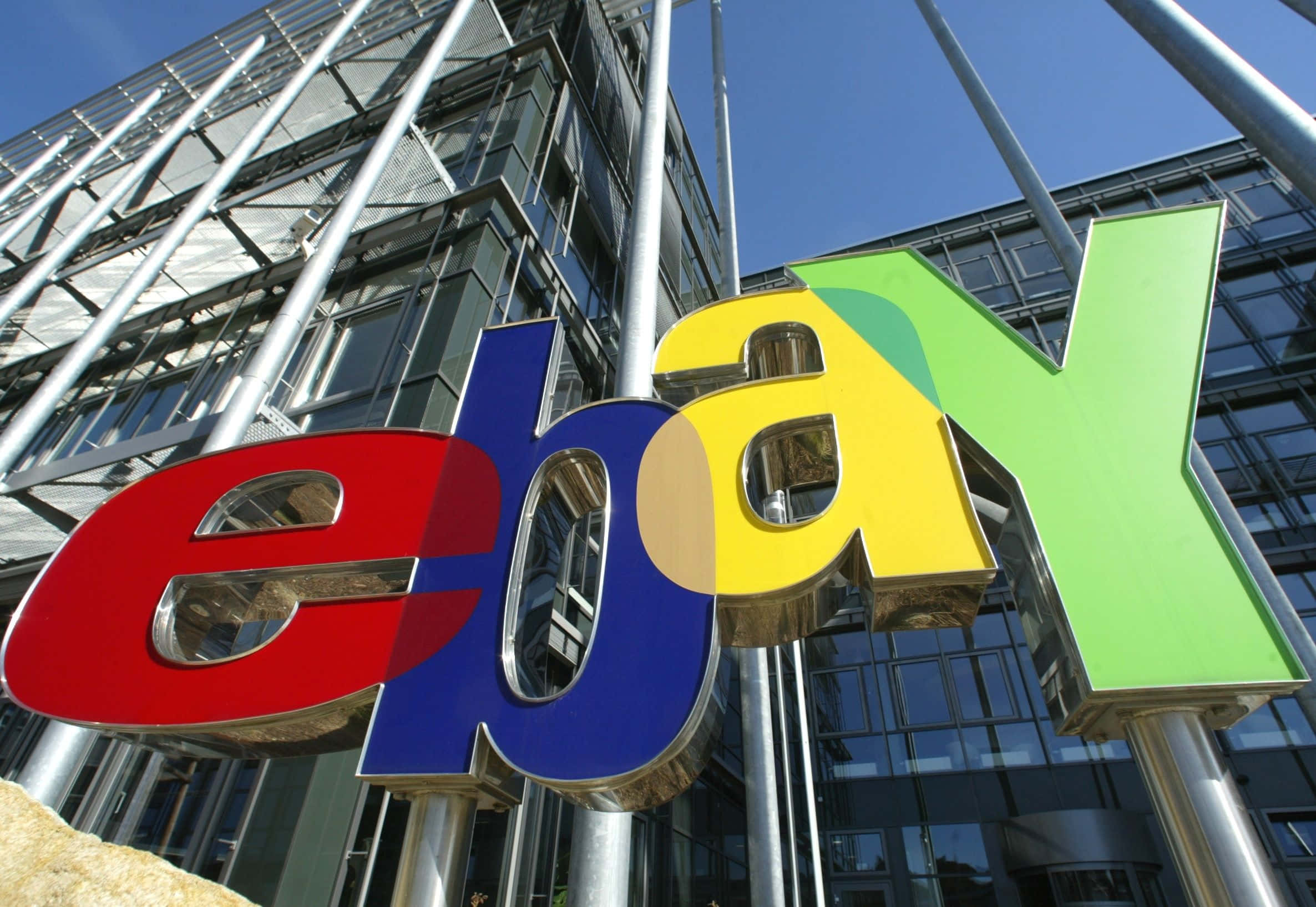 eBay 桌布 壁紙 — 色彩繽紛的大型eBay標誌字母，在晴朗的藍天下矗立於現代玻璃建築前。