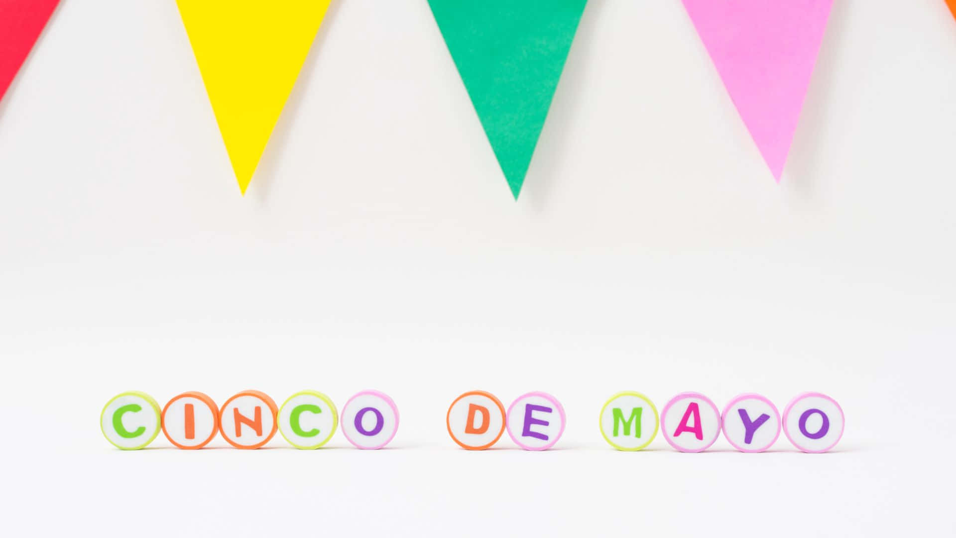 Cinco De Mayo 桌布 壁紙 — 色彩繽紛的字母瓷磚在乾淨的白色背景上，在一個充滿活力的三角形橫幅下面拼出「CINCO DE MAYO」。