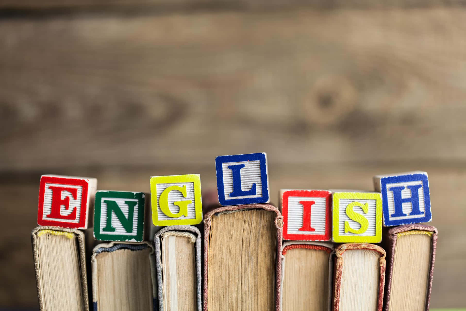 English 桌布 壁紙 — 色彩繽紛的字母積木拼出「ENGLISH」，放在一排復古書籍上，背景是質樸的木質背景。