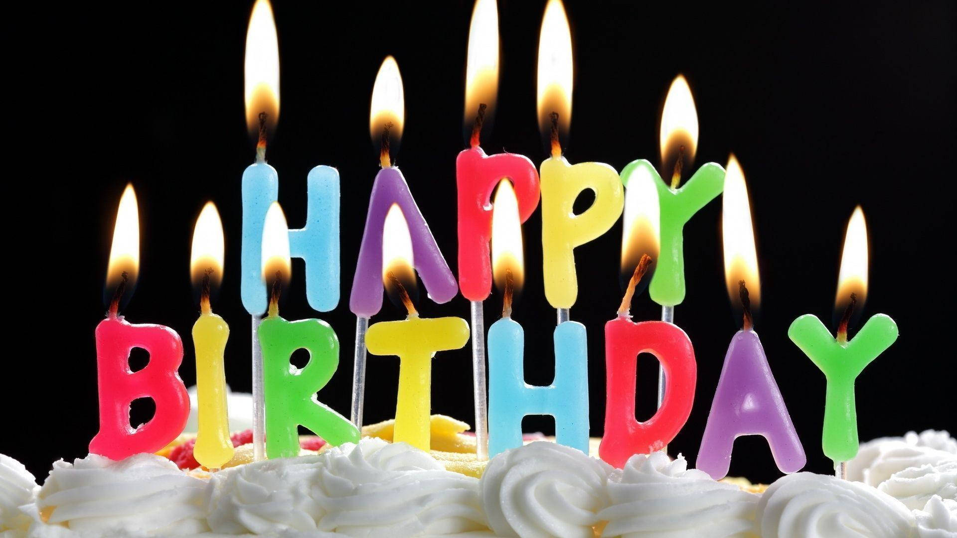 Birthday 桌布 壁紙 — 色彩繽紛的字母蠟燭拼出 happy birthday，在黑色背景上的糖霜蛋糕上溫暖地發光。