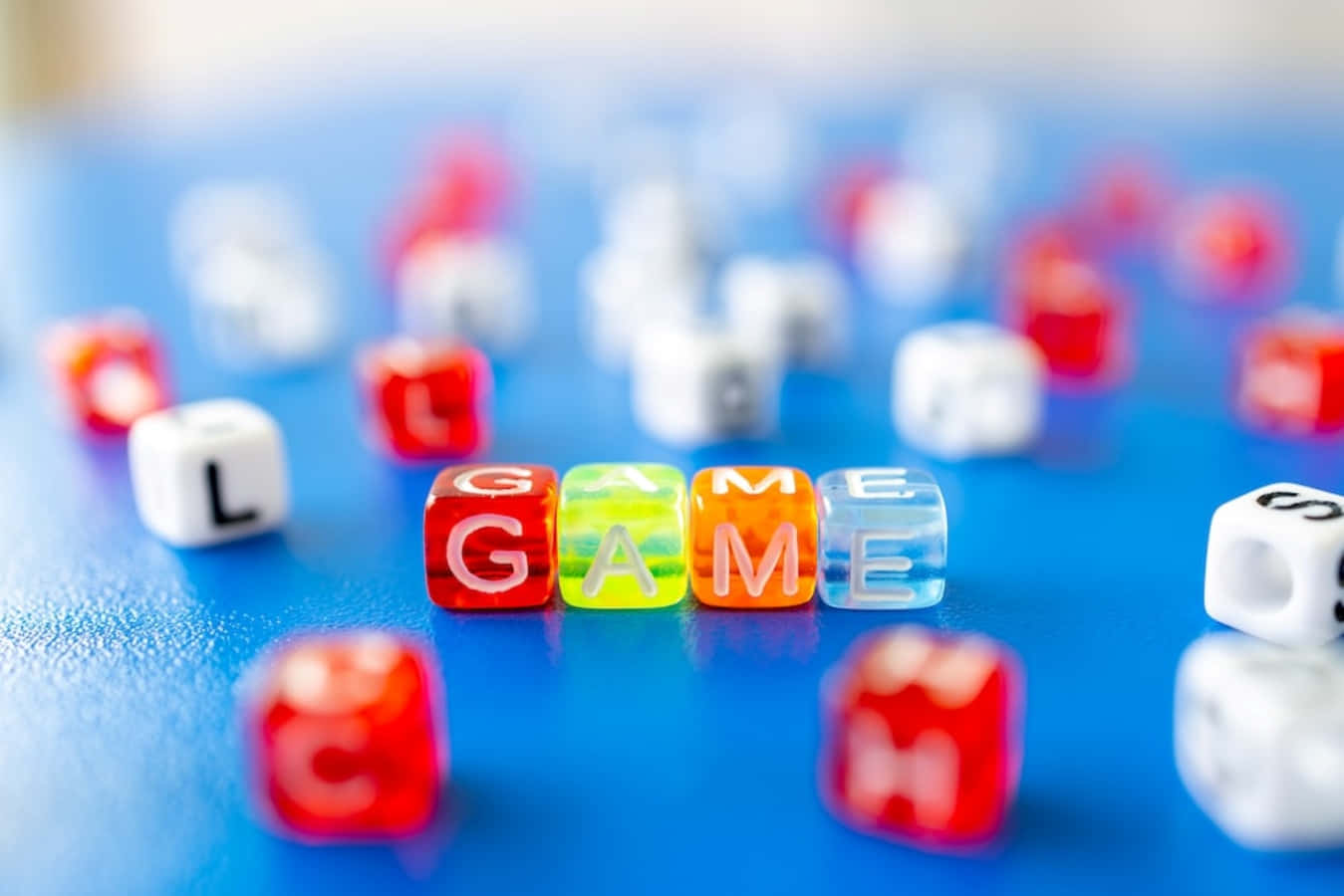 game 桌布 壁紙 — 色彩繽紛的字母骰子在充滿活力的藍色表面上拼出GAME，周圍散落紅色和白色骰子，呈現柔和焦點。