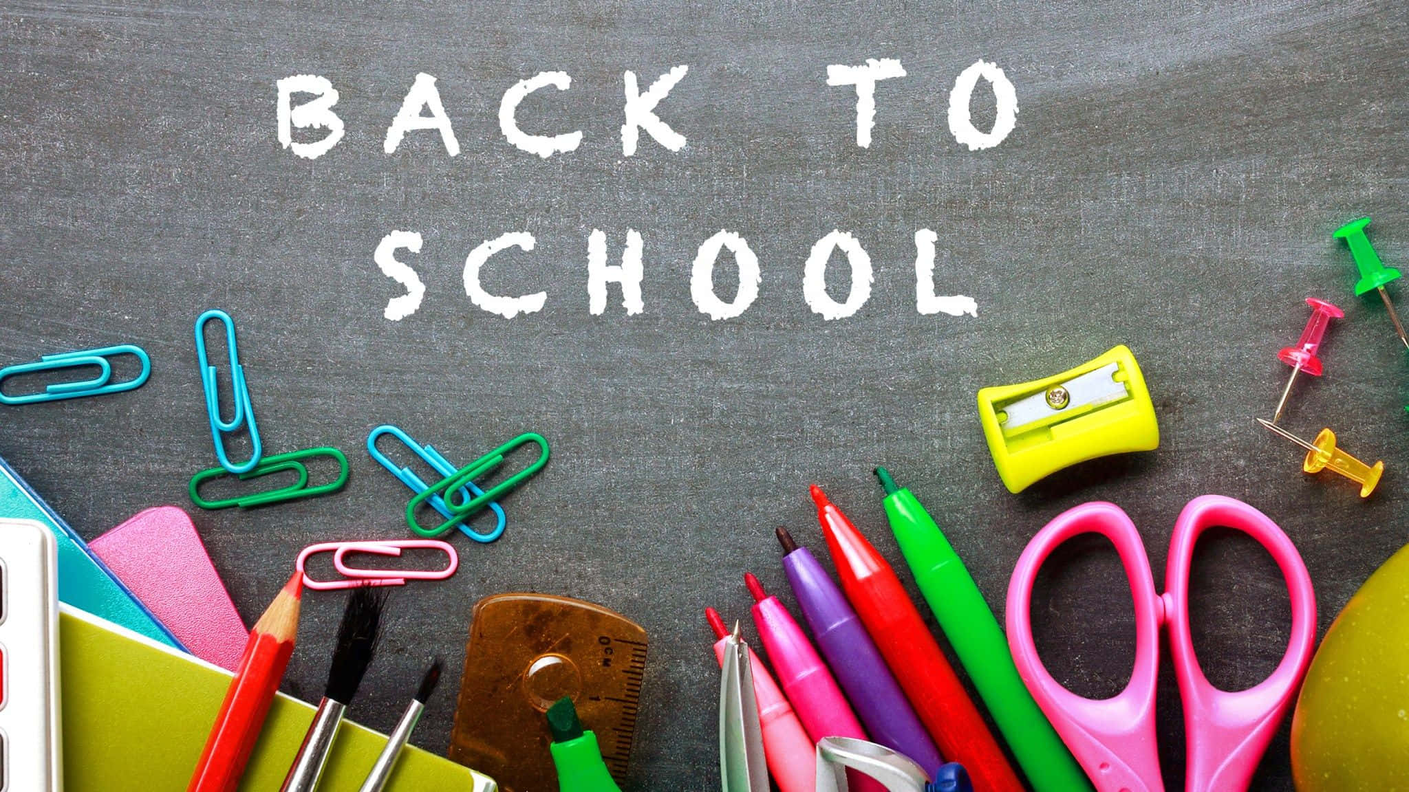Back To School 桌布 壁紙 — 色彩繽紛的學校用品，如剪刀、鉛筆和迴紋針，排列在黑板上，並用粉筆寫上「BACK TO SCHOOL」。