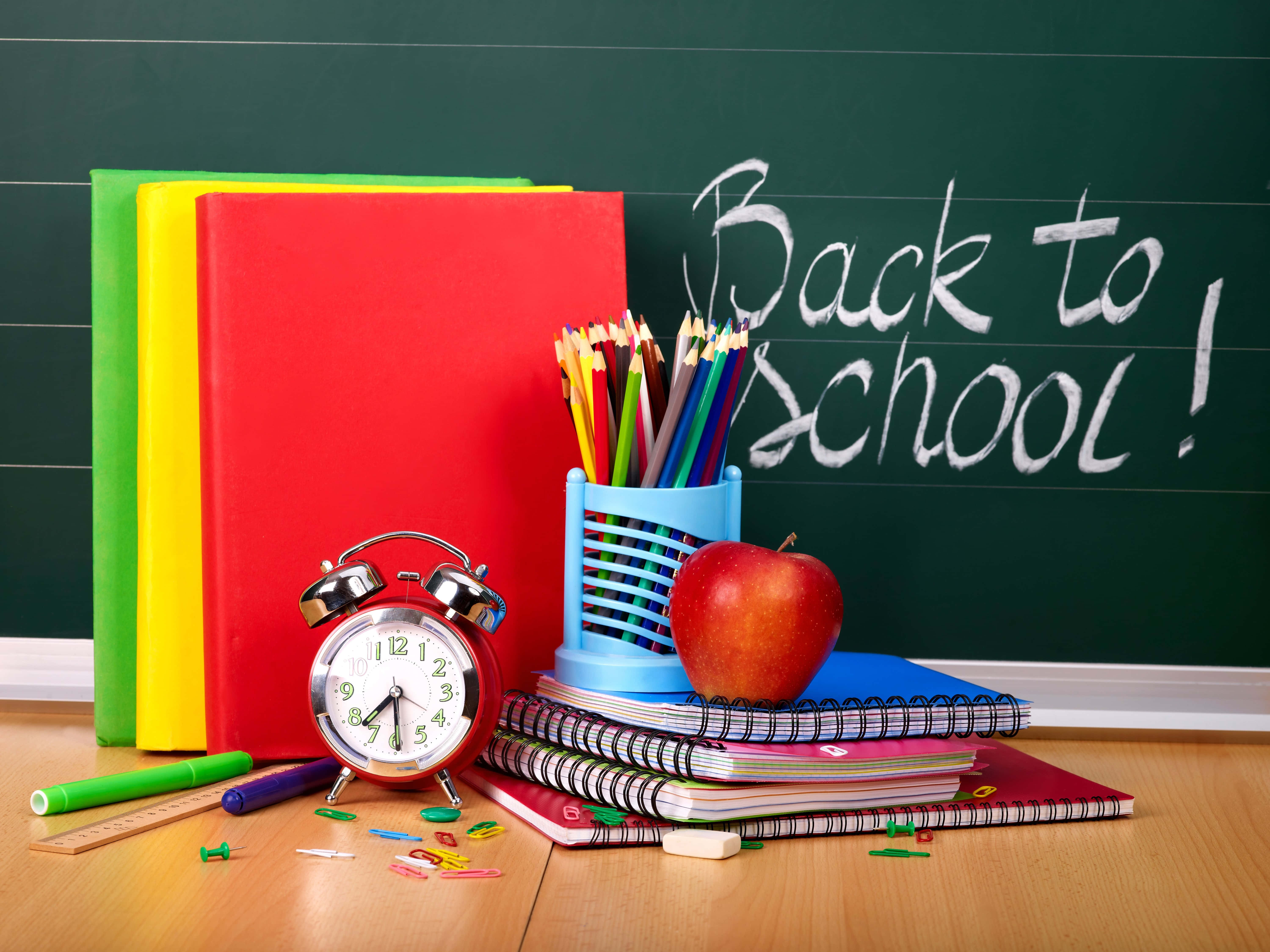 Back To School 桌布 壁紙 — 色彩繽紛的學校用品擺放在木桌上，後面有一塊寫著「Back to School!」的黑板。