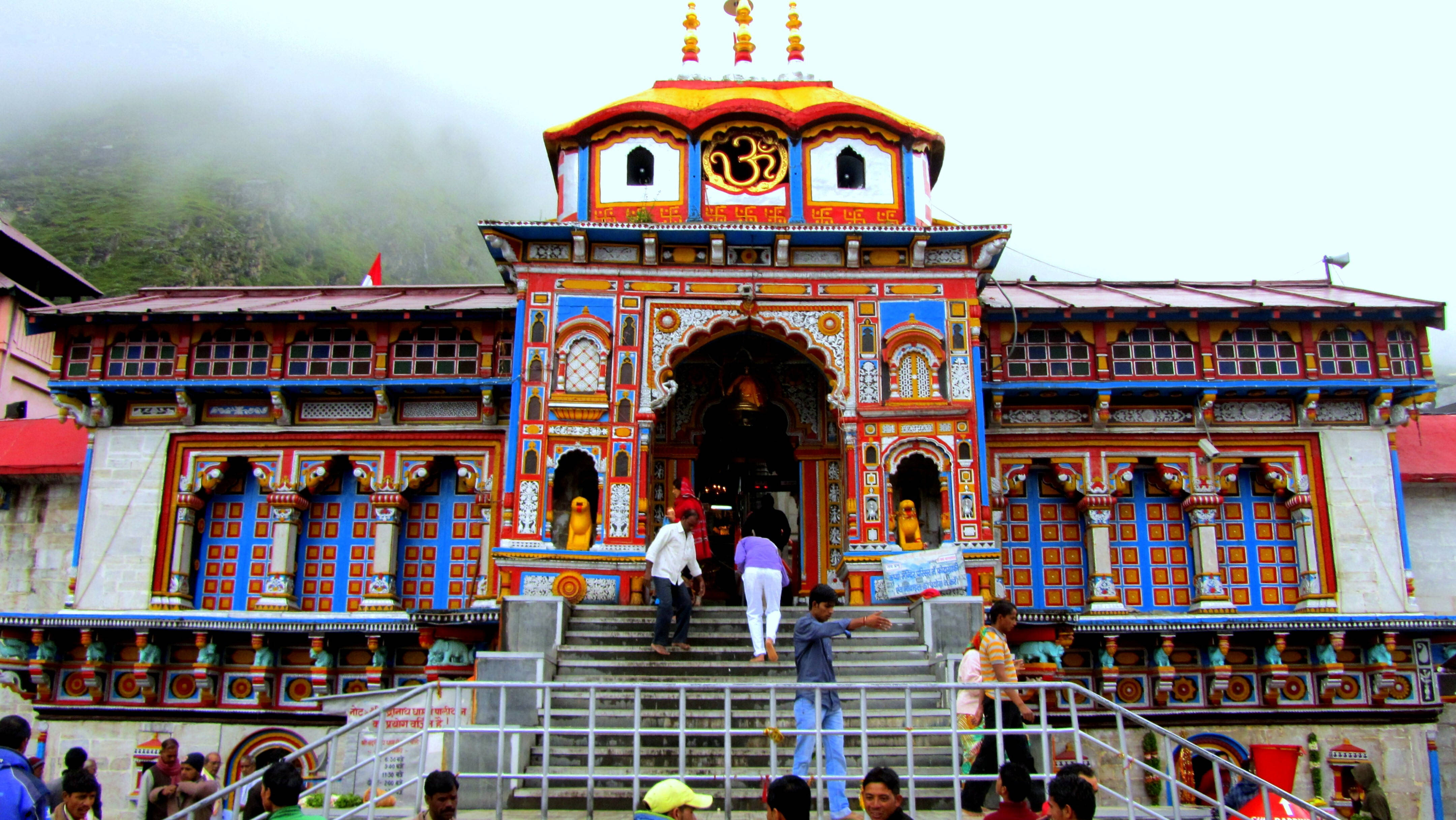 Kedarnath 桌布 壁紙 — 色彩繽紛的寺廟，帶有複雜的圖案和金色尖塔，矗立在霧氣繚繞的山巒之中，信徒們正攀登石階。