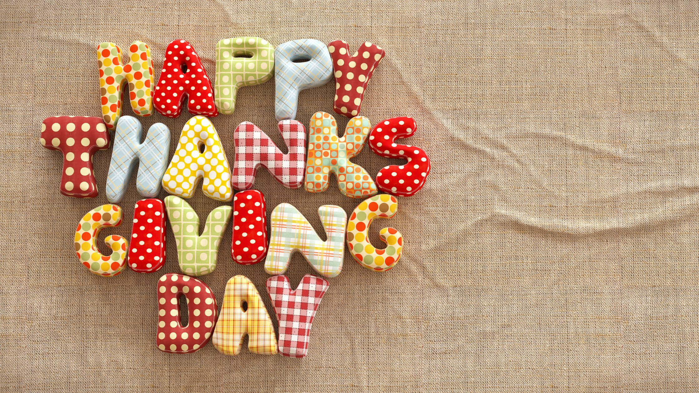 Thanksgiving Desktop 桌布 壁紙 — 色彩繽紛的布料字母拼出「HAPPY THANKSGIVING DAY」，排列在有紋理的米色粗麻布背景上。