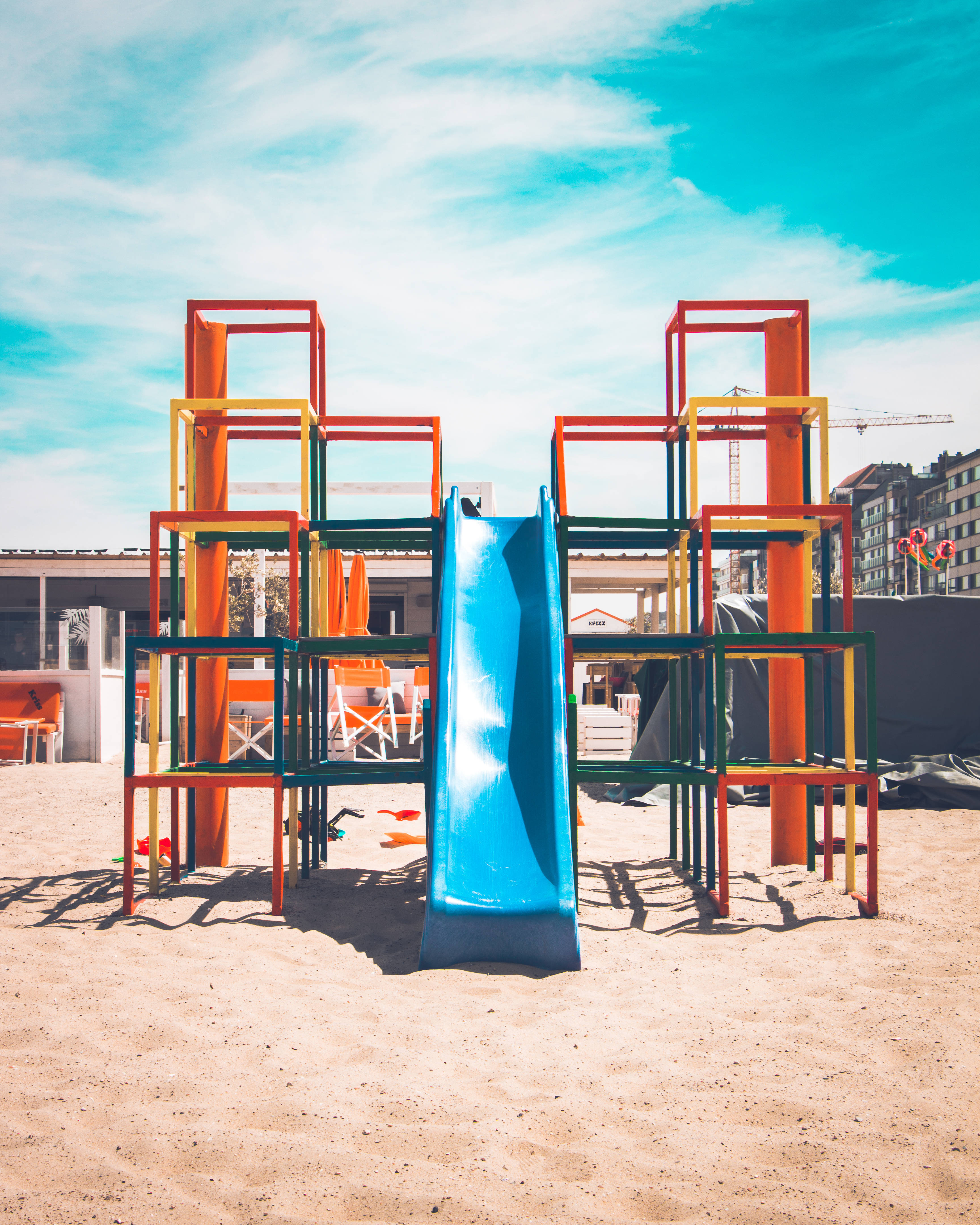 Playground 桌布 壁紙 — 色彩繽紛的幾何遊樂場結構，藍色溜滑梯矗立在沙地上，上方是明亮的藍天。